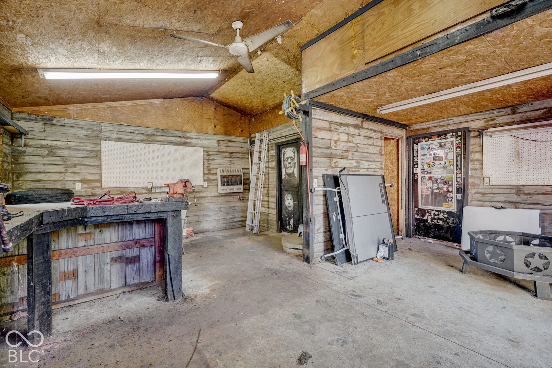 Detached workshop featuring wood-paneled walls, a built-in heavy-duty workbench, overhead lighting, a ceiling fan, and concrete flooring