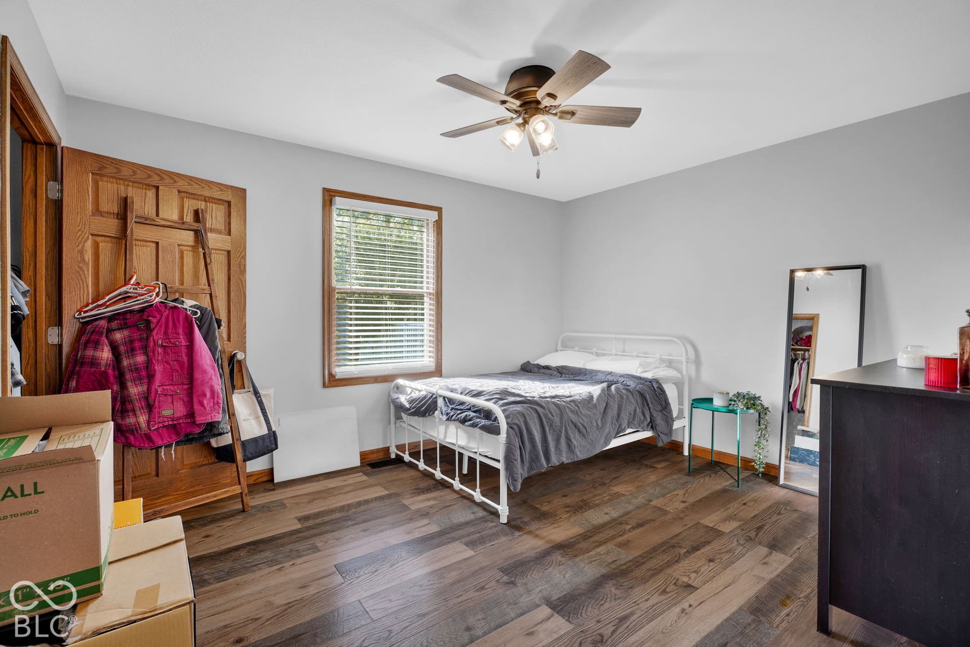 Room featuring wood-finish flooring, multi-pane window with wood-trim casing, and a ceiling-mounted fan with integrated lighting