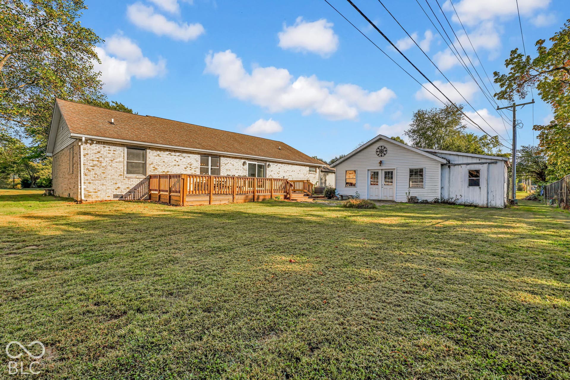 Expansive backyard featuring a manicured lawn, multi-level wood deck, white brick exterior, and detached outbuilding with double-door entry