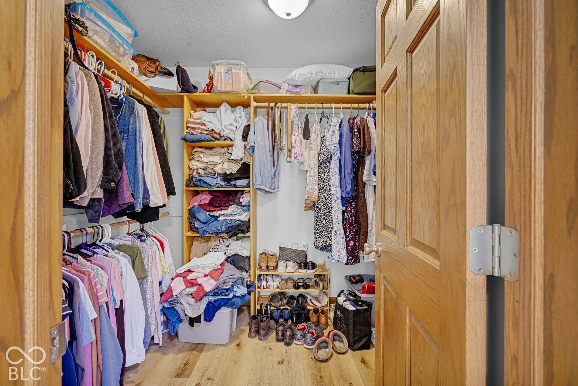 Walk-in closet featuring wood-finish flooring, built-in floor-to-ceiling wooden shelving, and dual-level hanging rods