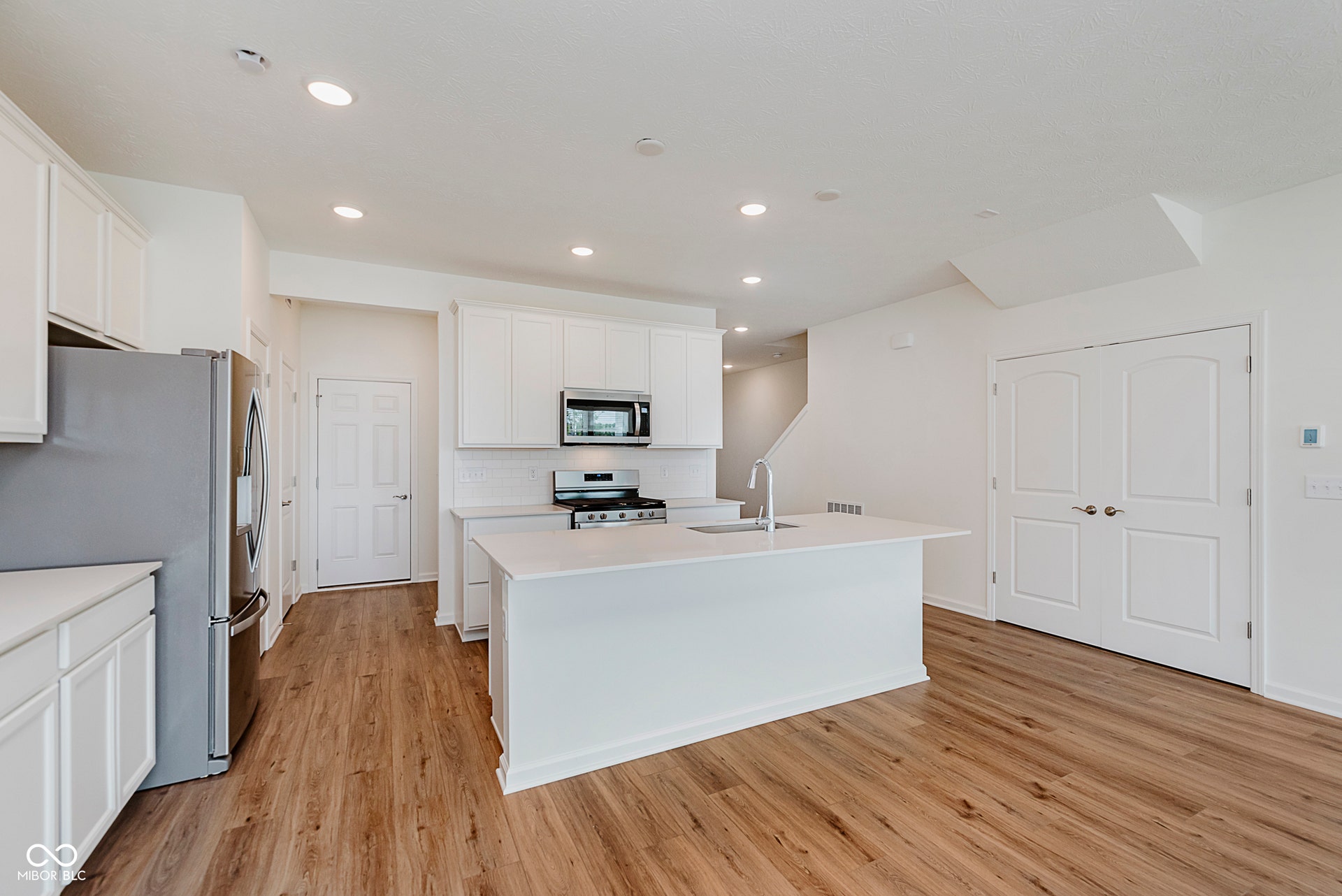 kitchen with stainless steel appliances, white cabinetry, an island with sink, recessed lighting, and light wood-style flooring