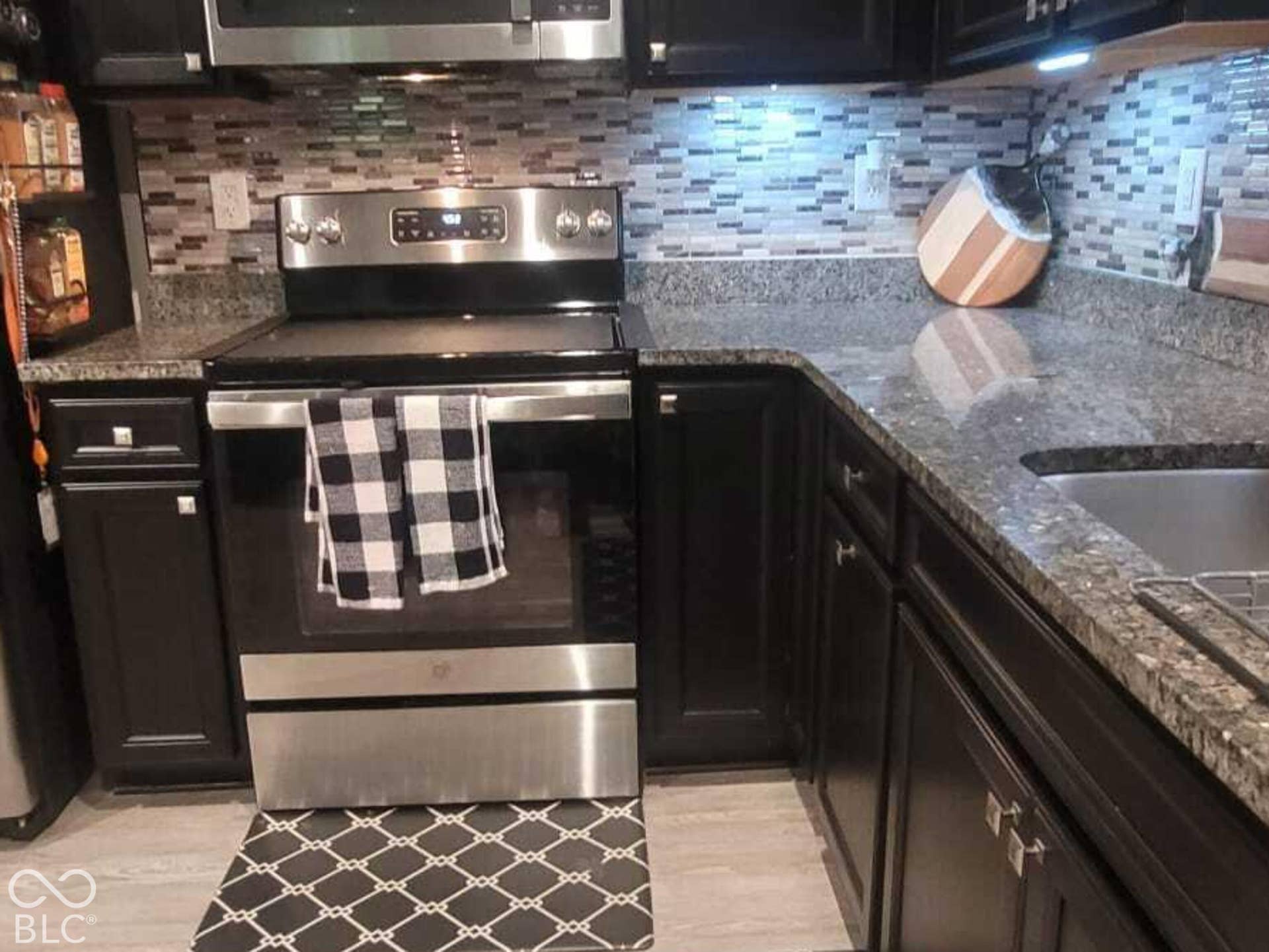 Kitchen featuring dark cabinetry, stainless steel appliances, stone-surface countertops, and a textured tile backsplash