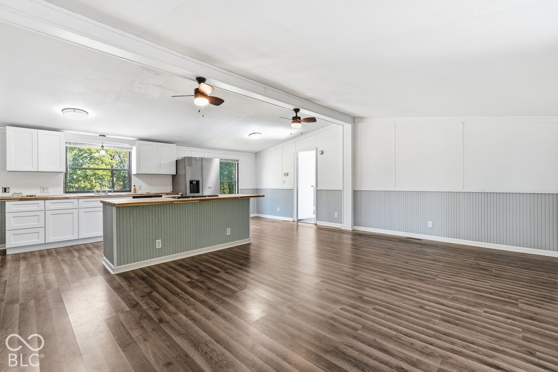 Kitchen featuring white shaker-style cabinetry, wood-finish flooring, a beadboard-paneled center island with a wood countertop, and dual ceiling fans