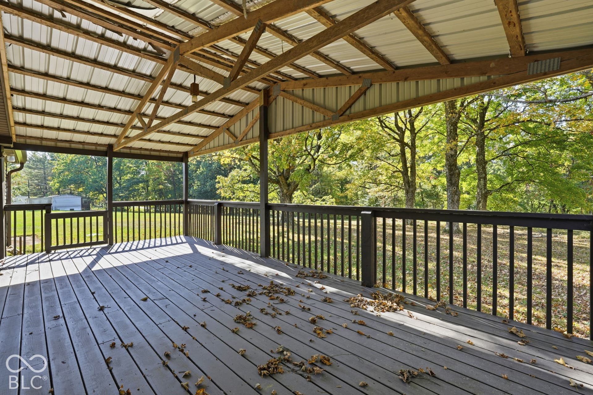 Covered deck featuring wood-finish decking, dark-toned railings, and an exposed wood-truss ceiling with metal roofing