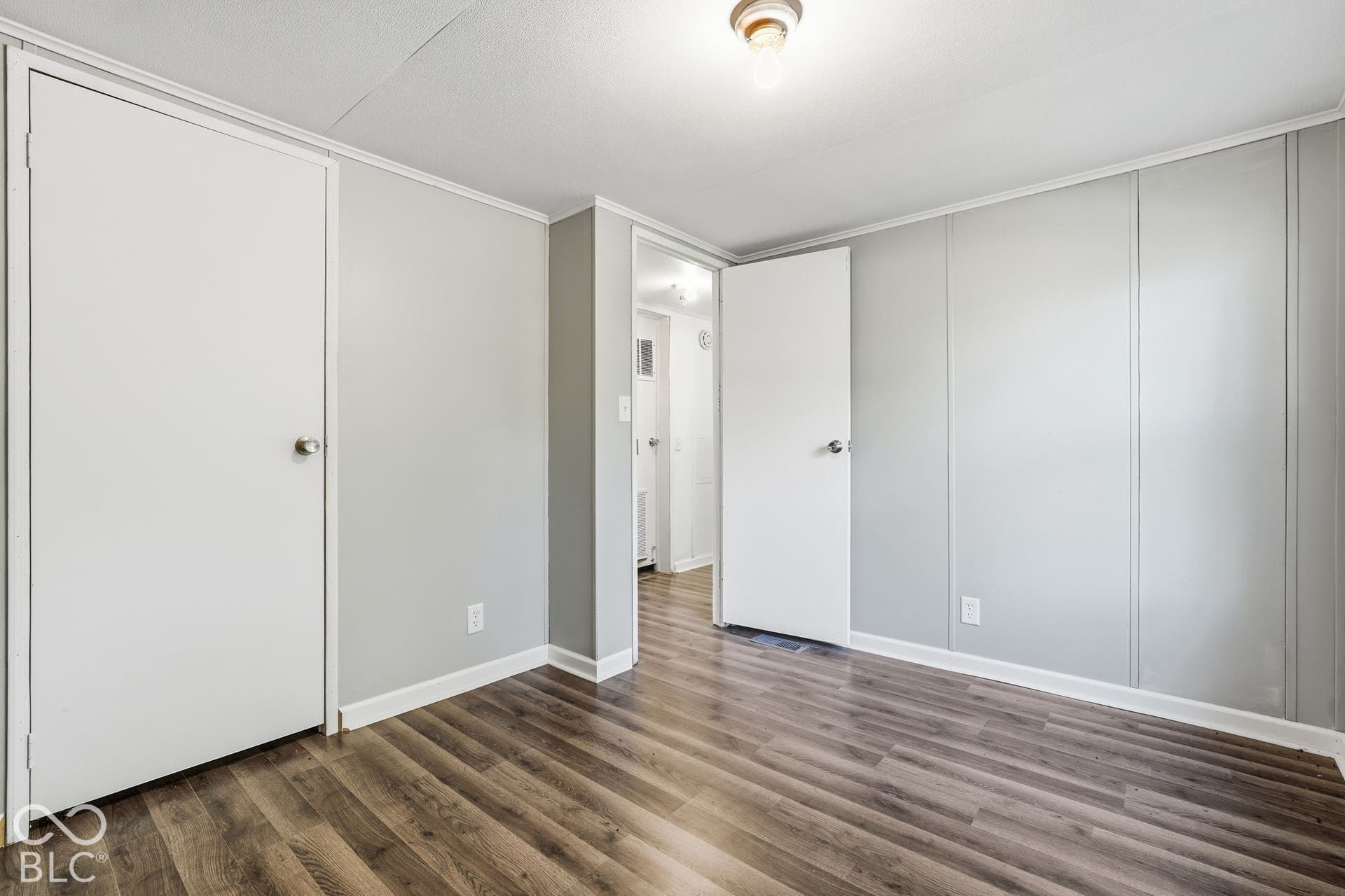 Room featuring wood-finish flooring, neutral panel walls, dual interior doors with metallic hardware, and a ceiling-mounted light fixture