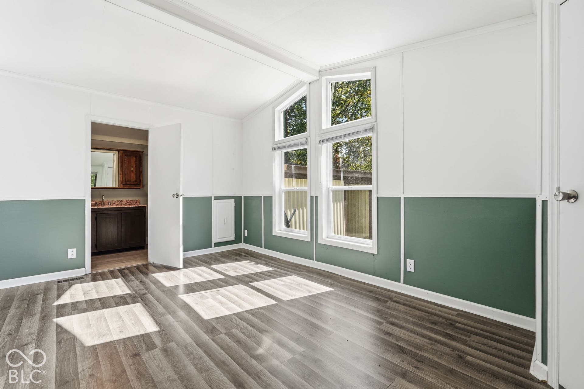 Room featuring two-tone wall treatments with wainscoting, wood-finish flooring, vaulted ceilings, and dual-pane windows