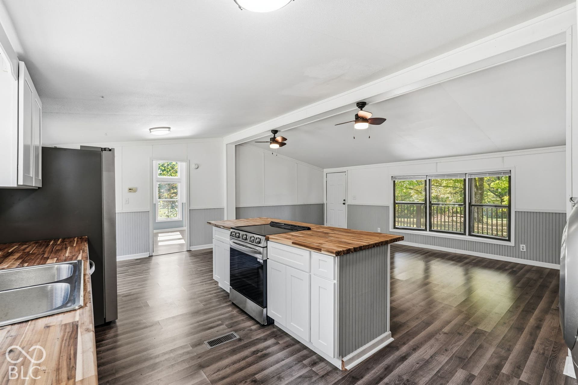 Kitchen featuring wood-finish flooring, white cabinetry with beadboard detailing, wood-top island with integrated stainless steel range, and dual ceiling fans