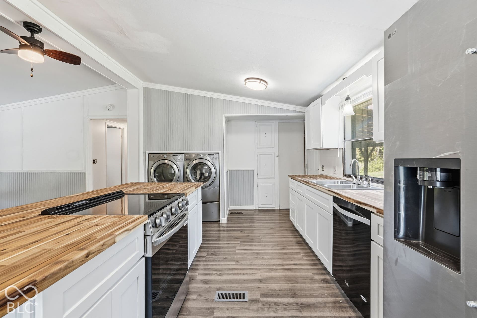 Kitchen featuring butcher block countertops, white shaker-style cabinetry, wood-finish flooring, stainless steel appliances, and integrated laundry area