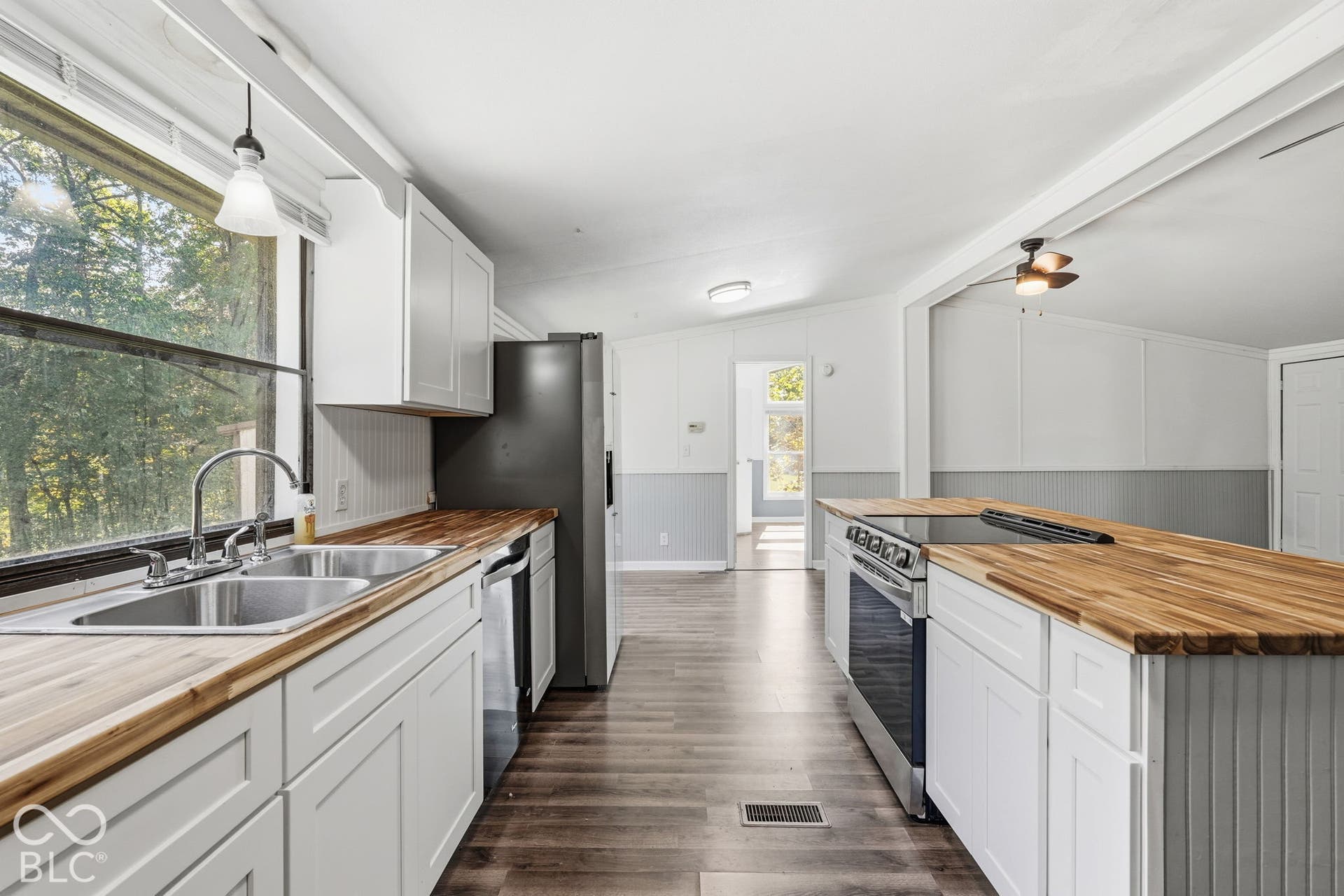 Kitchen featuring wood-finish countertops, white shaker-style cabinetry, wood-finish flooring, and a stainless steel double-basin sink