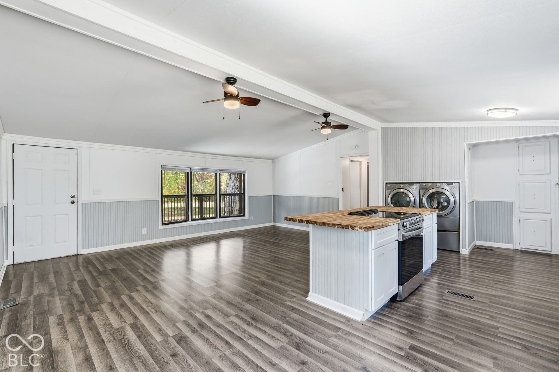 Open-concept interior featuring wood-finish flooring, dual ceiling fans, beadboard wainscoting, and a kitchen island with a built-in range