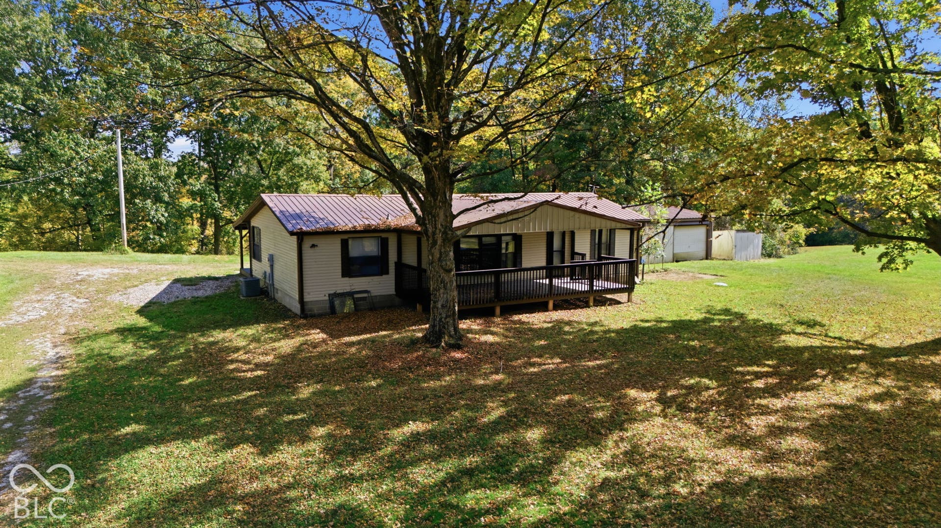 Single-story residence featuring a metal roof, front deck, and detached garage situated on a sprawling lot with mature trees