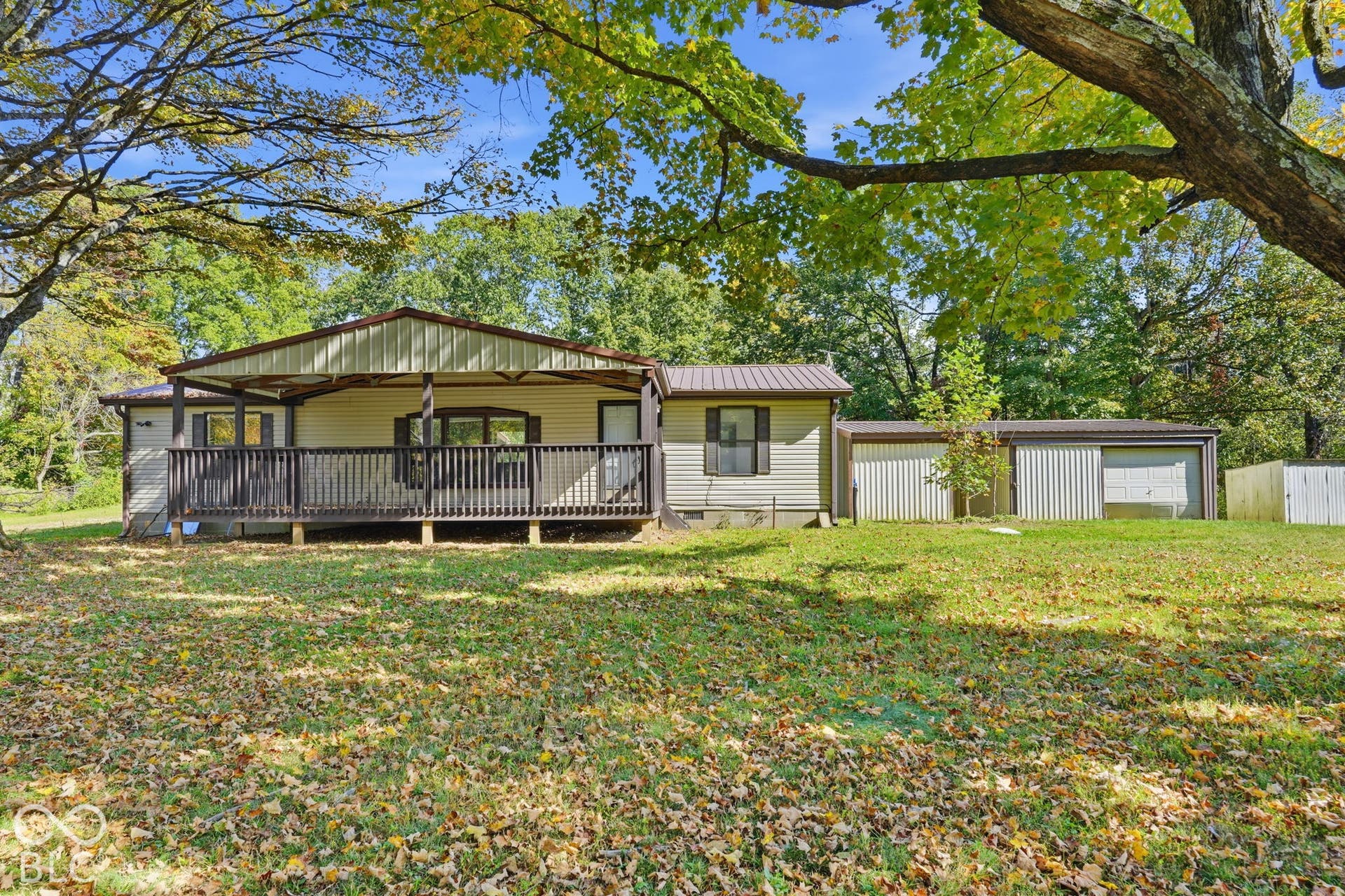 Single-story exterior featuring metal roofing, horizontal siding, a covered deck with railings, and an attached multi-car garage on a wooded lot