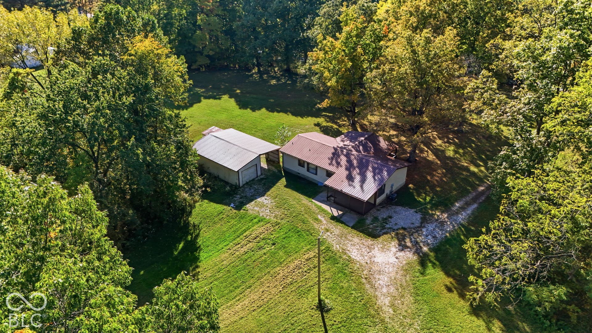 Detached structure with metal roofing, gravel driveway, expansive lawn, and mature tree canopy