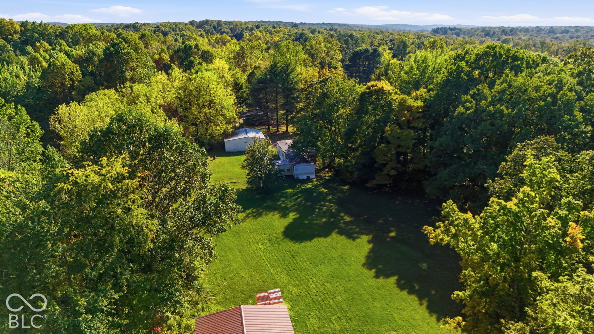Expansive parcel featuring large areas of cleared grass, mature tree coverage, and a detached outbuilding
