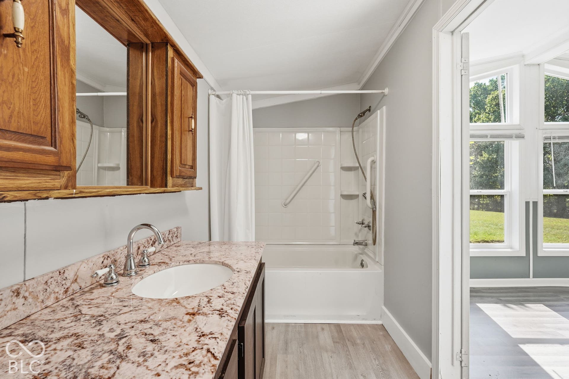 Bathroom featuring a stone-finish countertop, dual-handle faucet, wood-finish wall cabinetry, tub-shower combination with surround, and wood-finish flooring