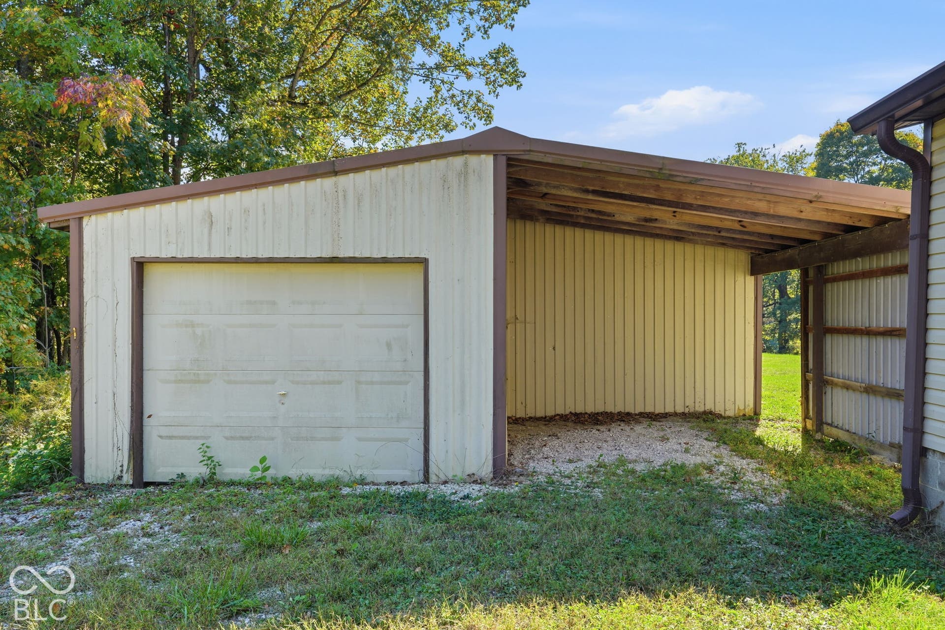 Detached structure featuring a metal-sided exterior, a single-bay garage with a roll-up door, and an open-air covered parking area