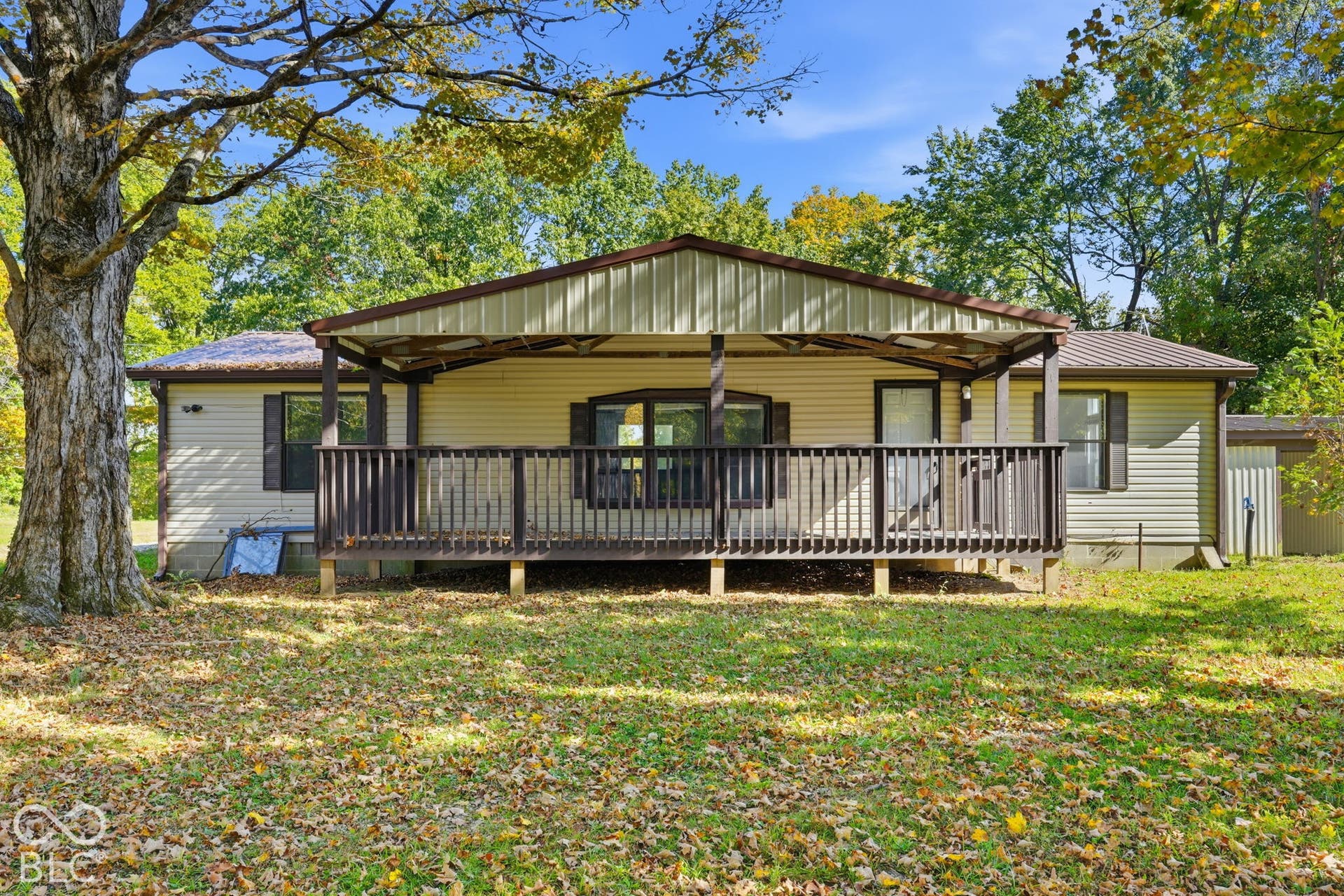 Single-story exterior featuring a metal-roofed covered porch, vinyl siding, shuttered windows, and a mature tree backdrop