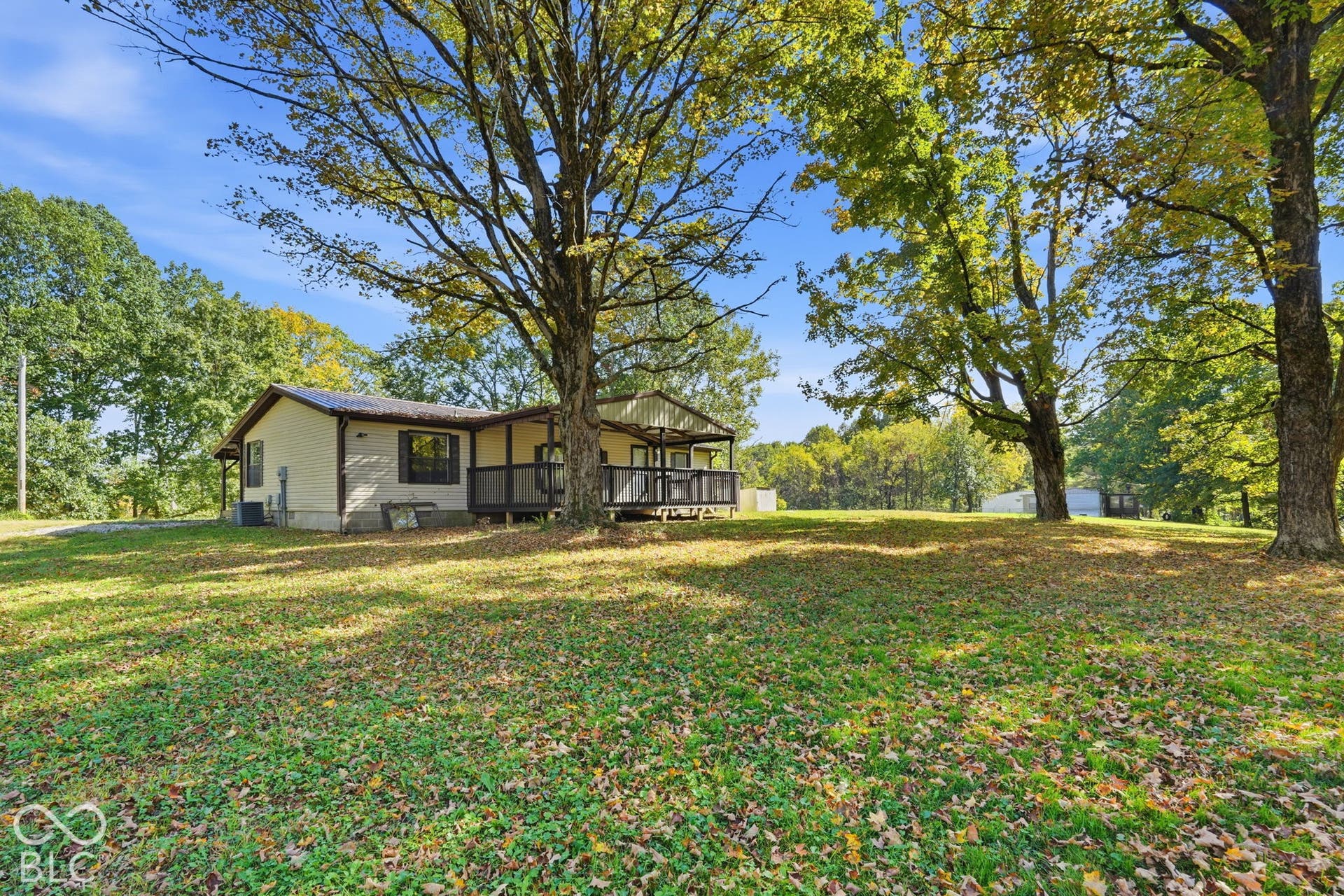 Single-story residence featuring light-toned exterior siding, a covered front porch with railings, and expansive grounds populated with mature trees