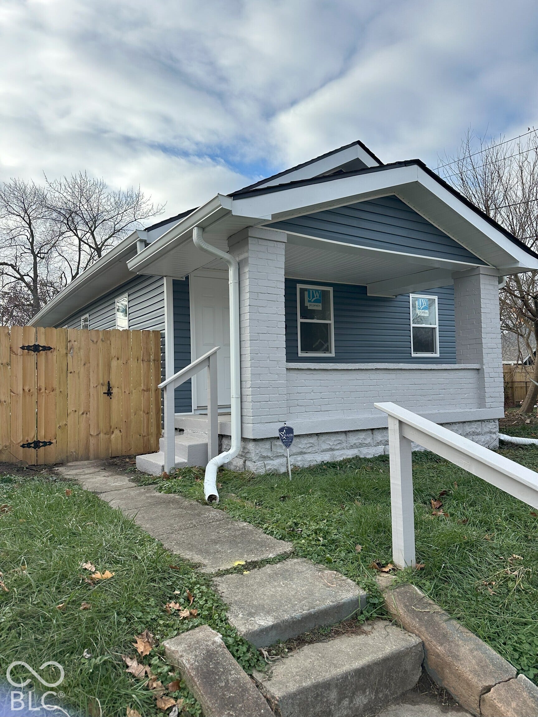 Exterior facade featuring horizontal siding, a covered front porch with painted brick columns, a stone foundation, and a wooden privacy fence