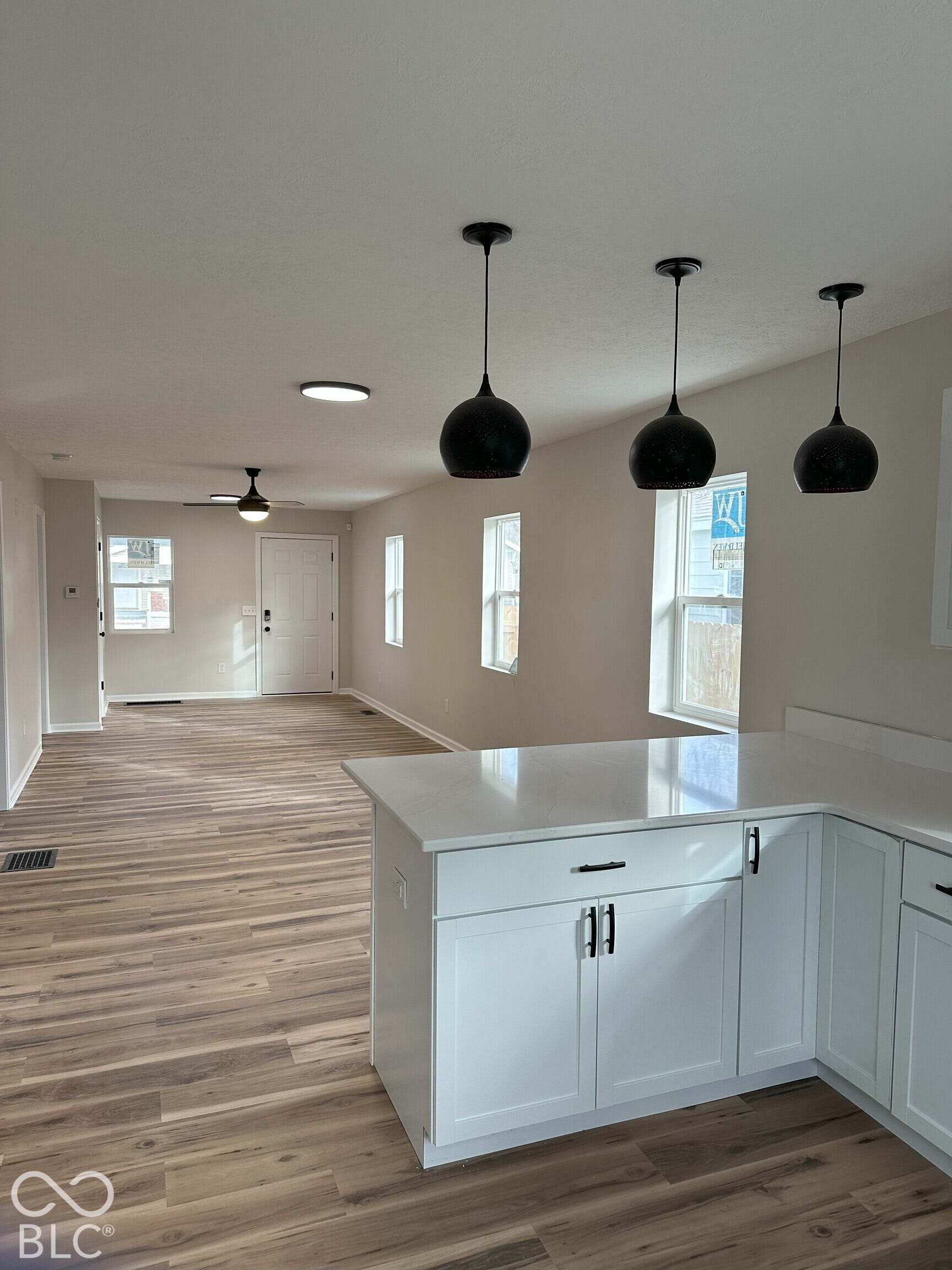 Kitchen featuring a quartz countertop, white cabinetry with matte black hardware, and three matte black pendant lights, complemented by wood-finish flooring throughout the space