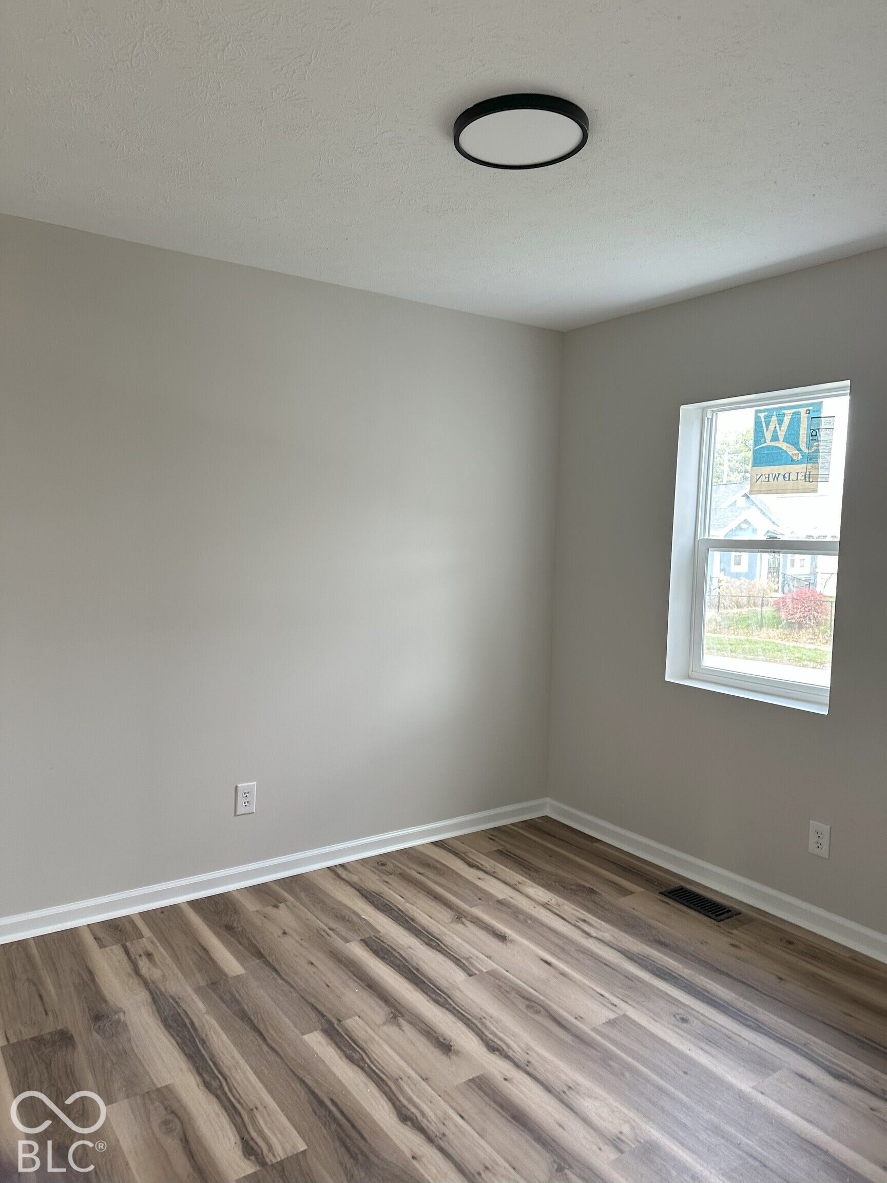 Neutral interior space featuring wood-finish flooring, a single-pane window, and a circular flush-mount ceiling light fixture