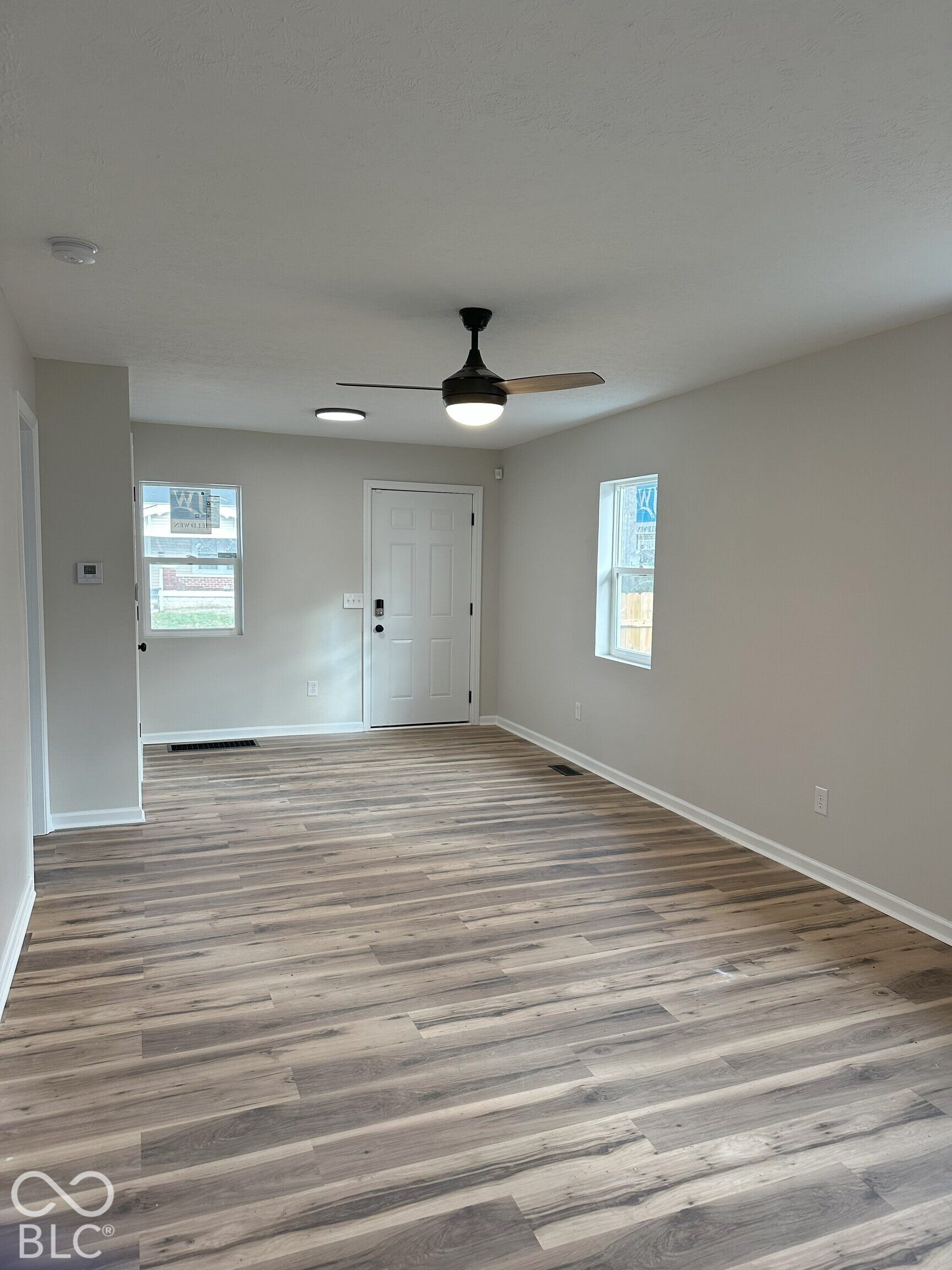Interior space featuring neutral wall paint, wood-finish flooring, a contemporary ceiling fan with integrated lighting, and dual vinyl-frame windows