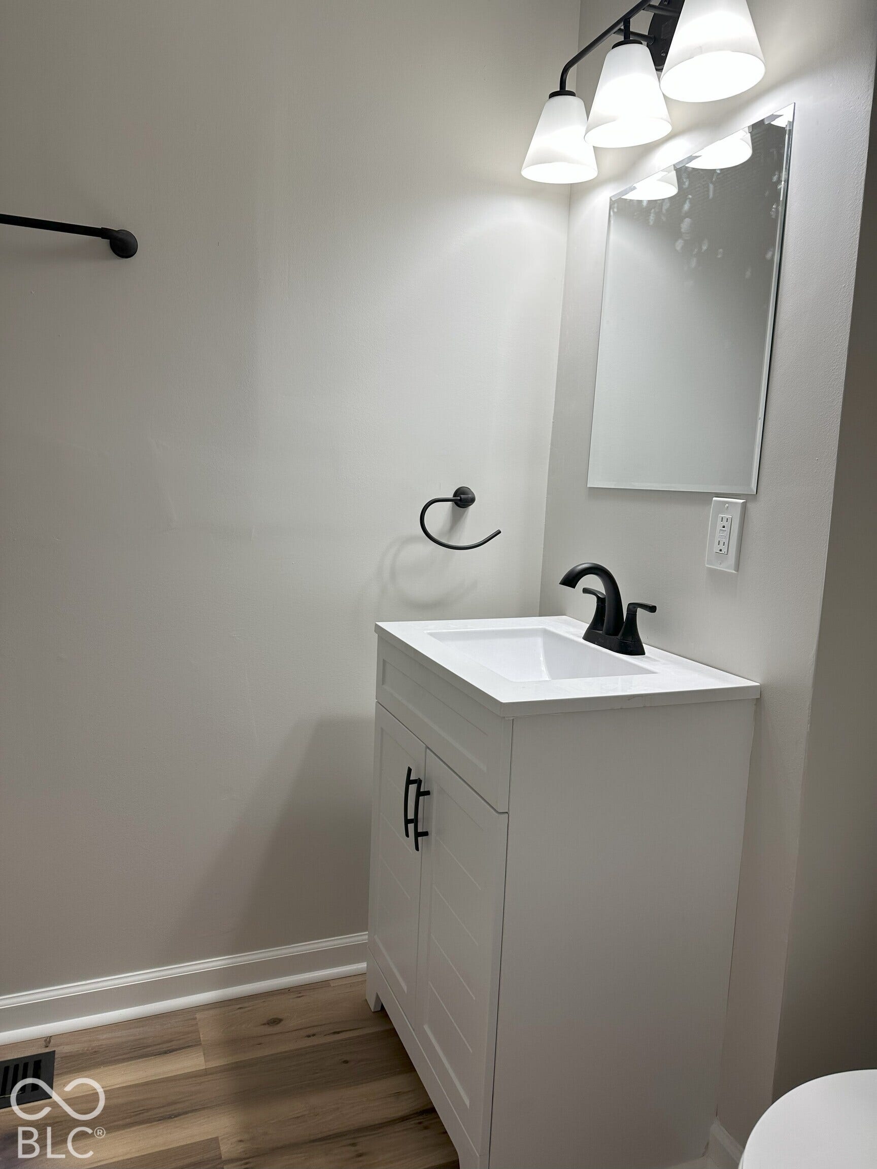White vanity with an integrated rectangular sink, matte black hardware, high-arc faucet, wall-mounted mirror, and wood-finish flooring