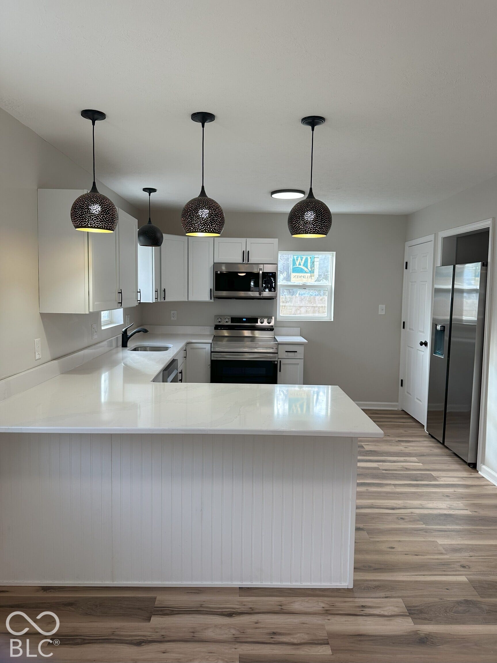 Kitchen featuring white cabinetry, solid surface countertops, wood-finish flooring, stainless steel appliances, and three metal pendant lights