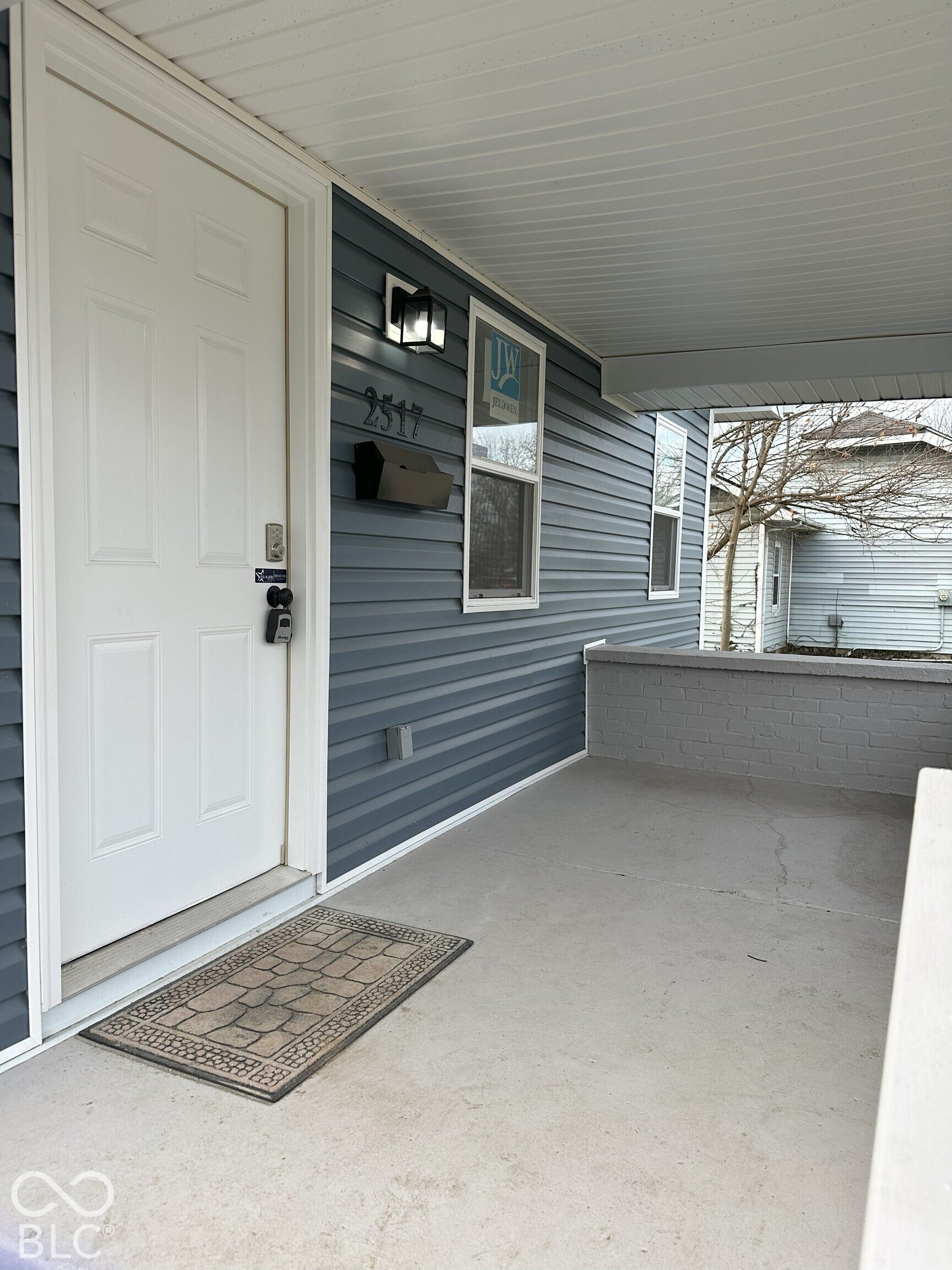 Covered front porch featuring dark blue horizontal siding, a white paneled door, a metal wall-mounted mailbox, and a geometric exterior light fixture