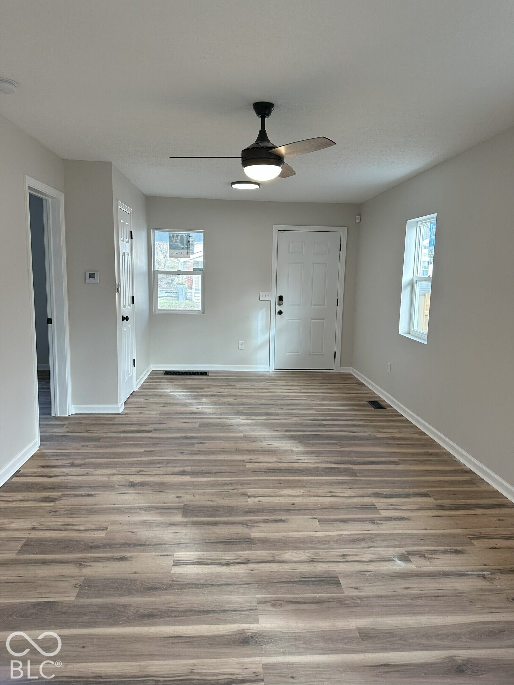 Interior space featuring wood-finish flooring, a neutral color palette, multiple windows, and a ceiling-mounted light fixture with a fan