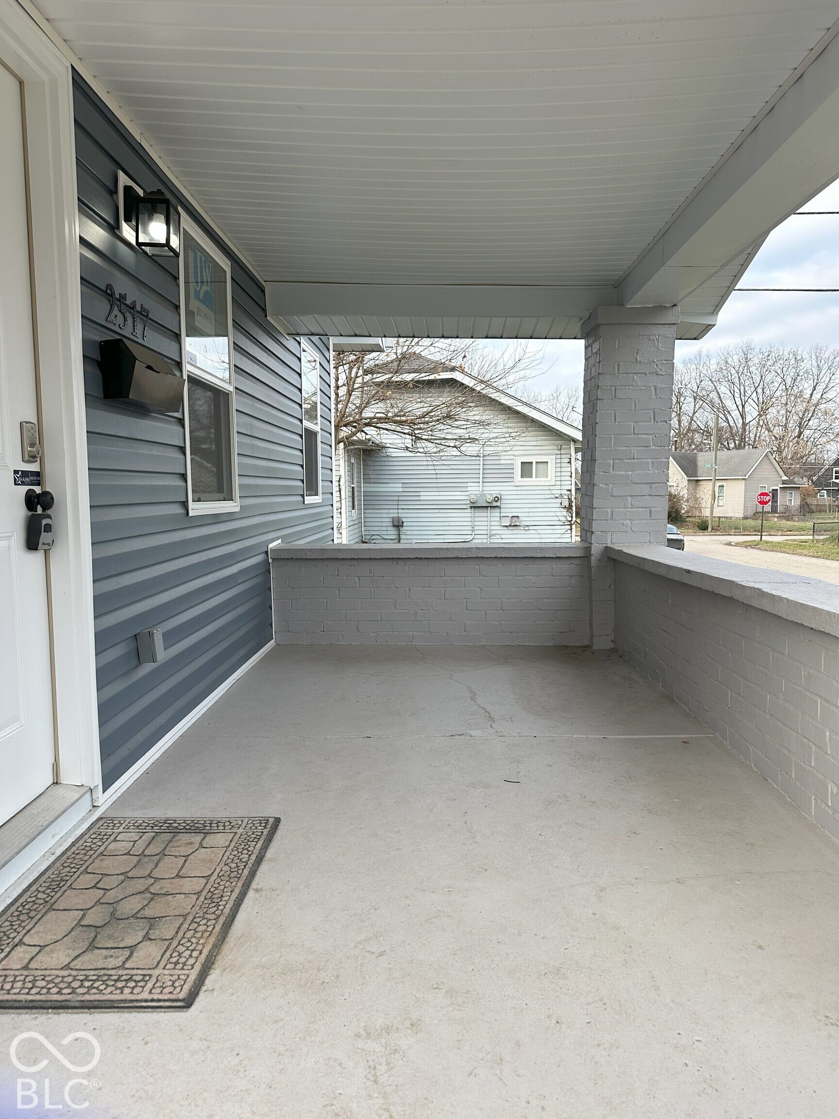 Covered front porch featuring horizontal lap siding, a painted brick knee wall, a solid porch pillar, and a wall-mounted exterior light fixture