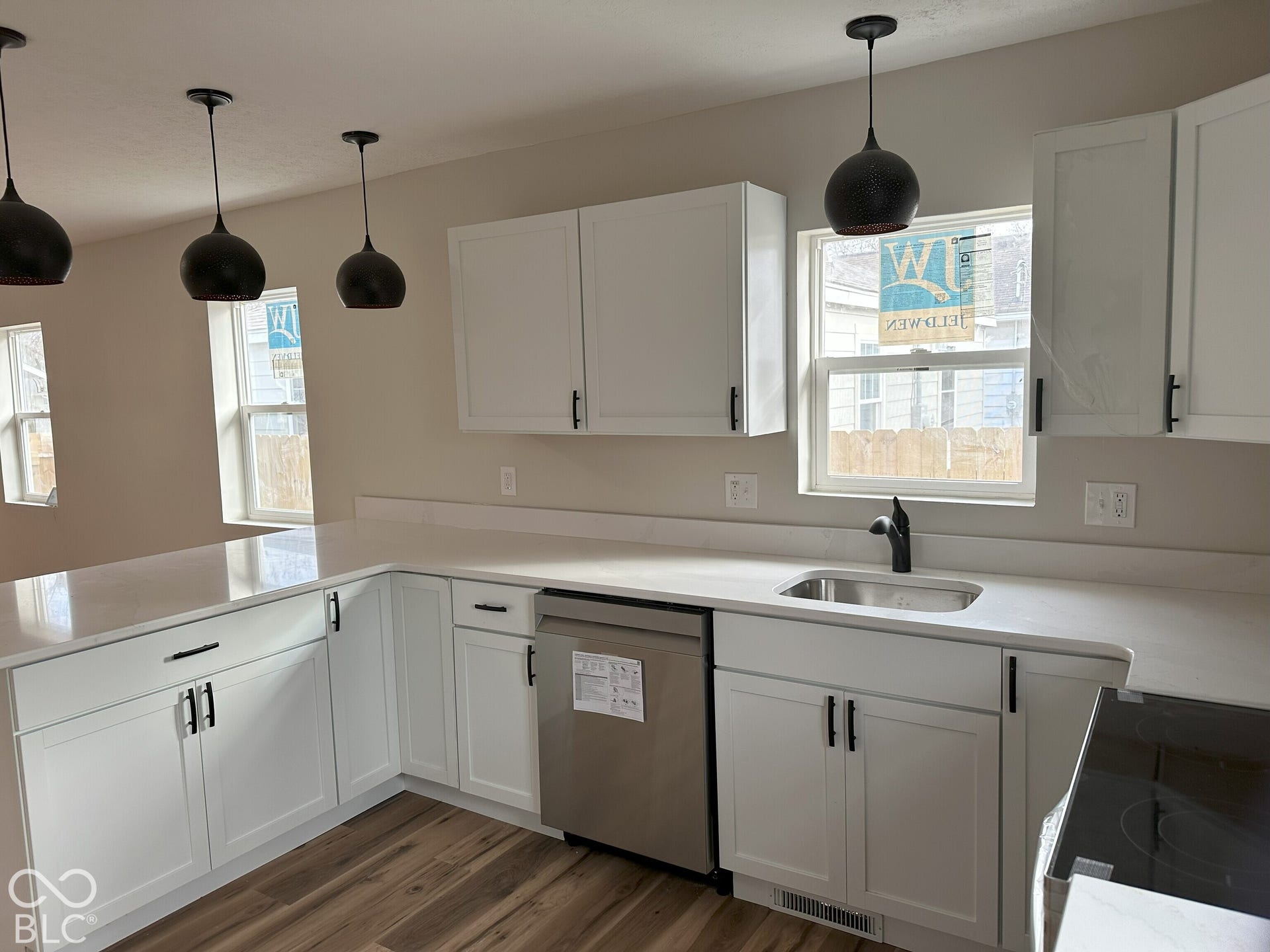 Kitchen featuring white shaker-style cabinetry, solid-surface countertops, stainless steel dishwasher, wood-finish flooring, and black pendant lighting