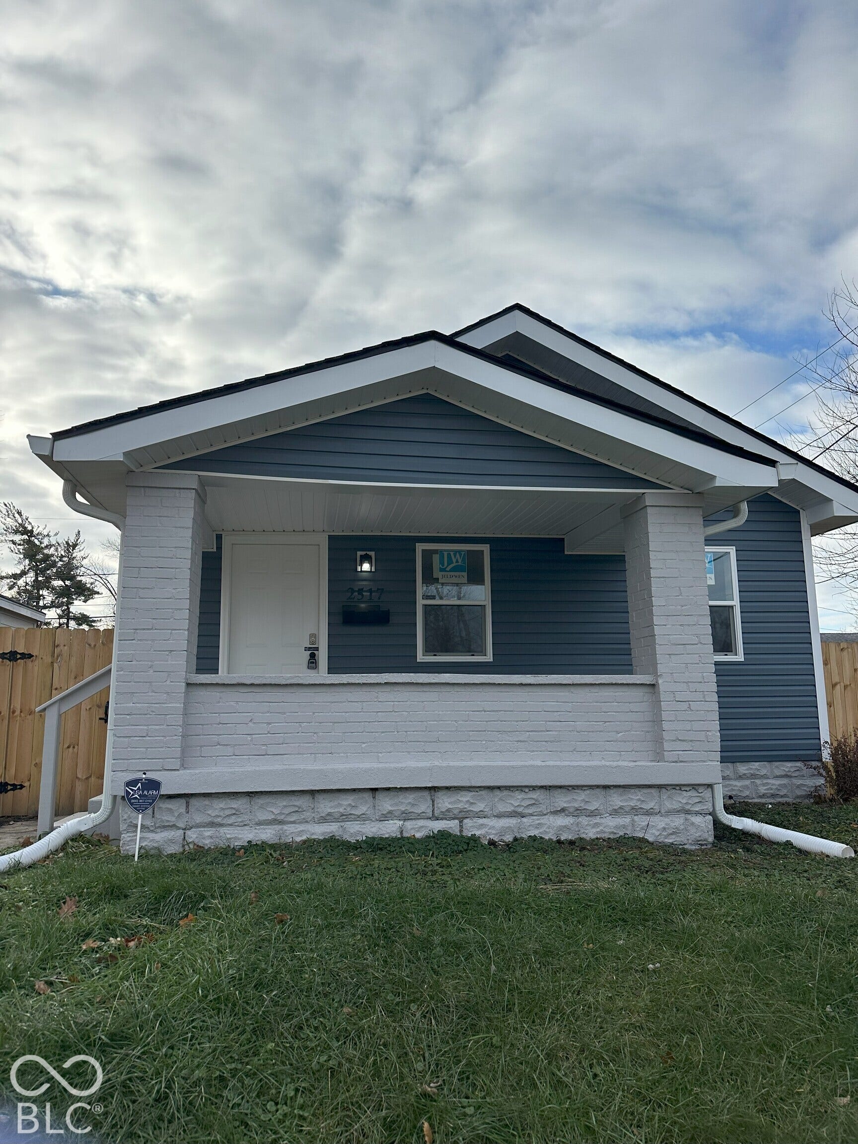Exterior featuring dark blue horizontal siding, a covered front porch with painted brick pillars, and a stone-faced foundation