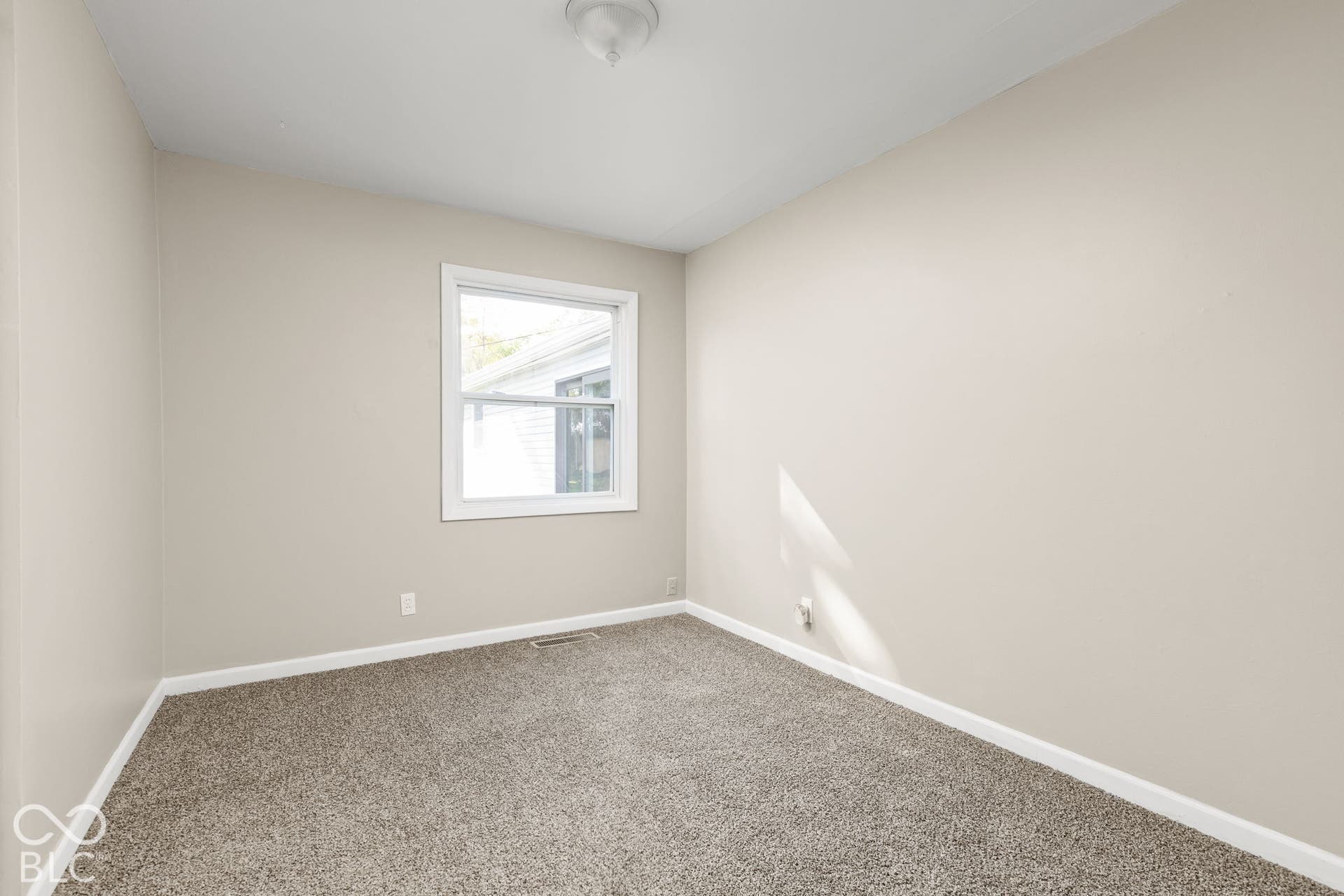 Neutral-toned interior space featuring wall-to-wall carpeting, a single-pane window with white trim, and a flush-mount ceiling light fixture