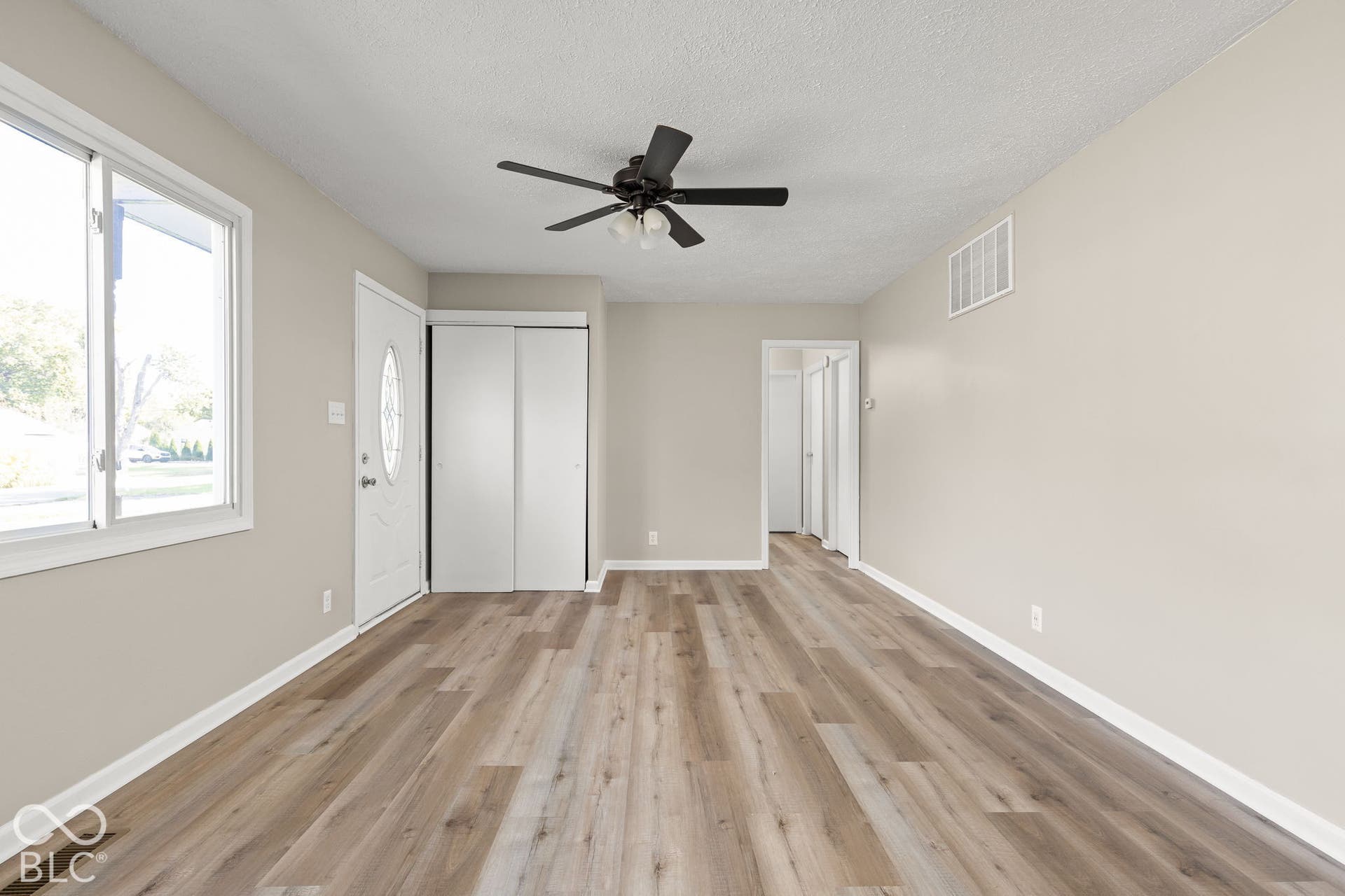 Neutral-toned interior featuring wood-finish flooring, a ceiling fan with integrated lighting, dual-panel closet doors, and an exterior door with an oval glass insert