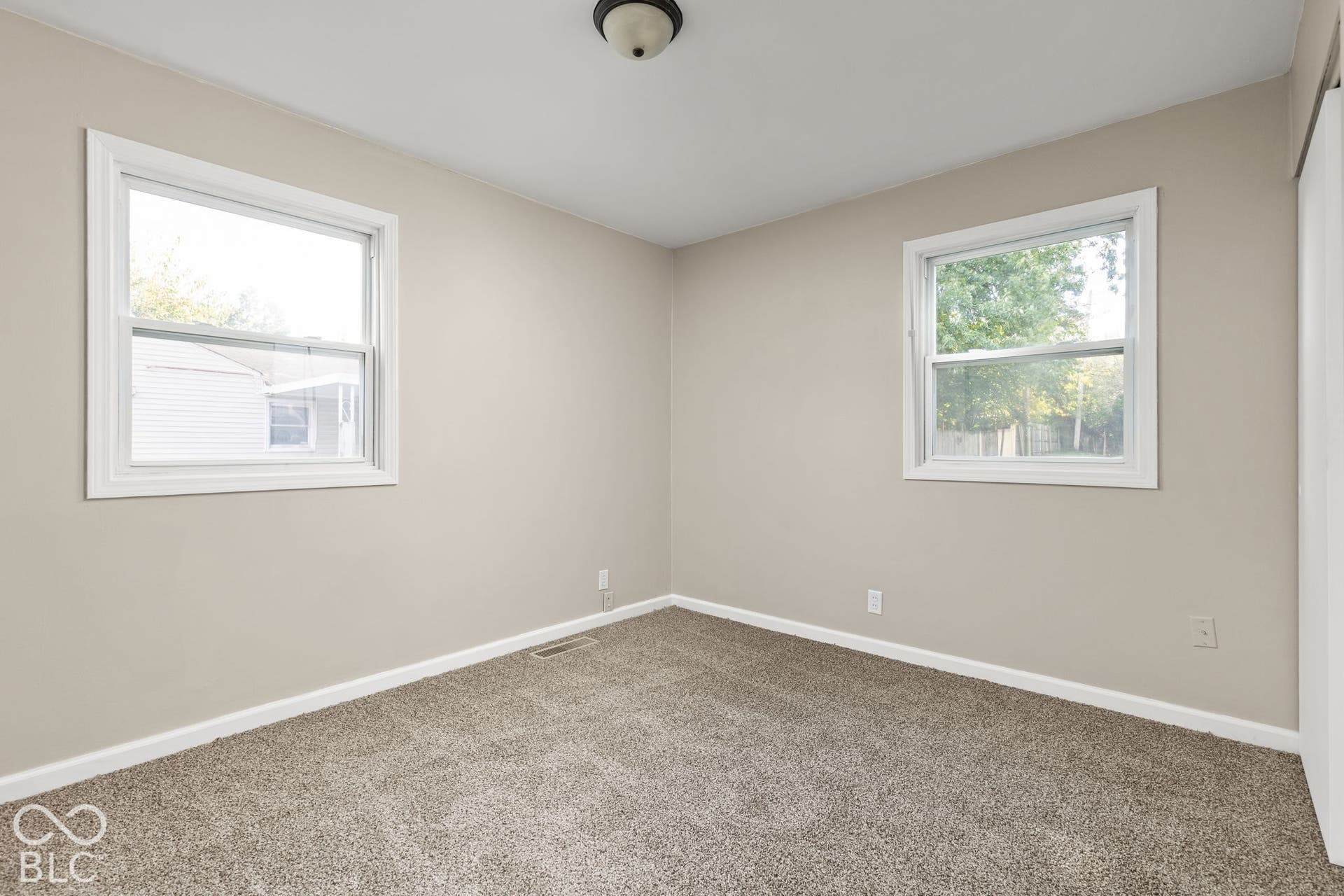 Room featuring neutral wall paint, two dual-pane windows with white trim, carpeting, and a flush-mount ceiling light fixture