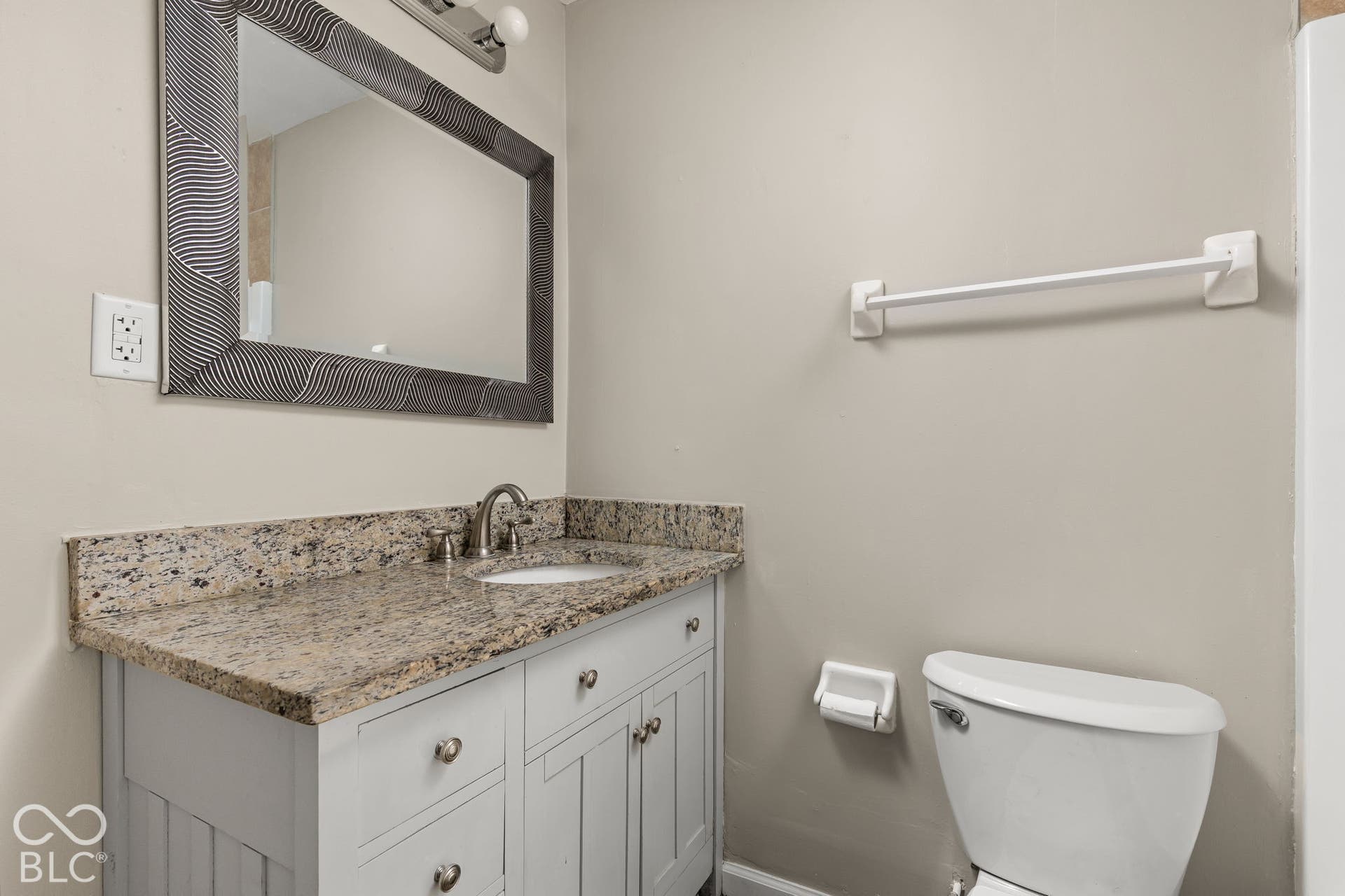 Bathroom featuring a vanity with stone-finish countertop, undermount sink, brushed nickel faucet, and a wall-mounted framed mirror