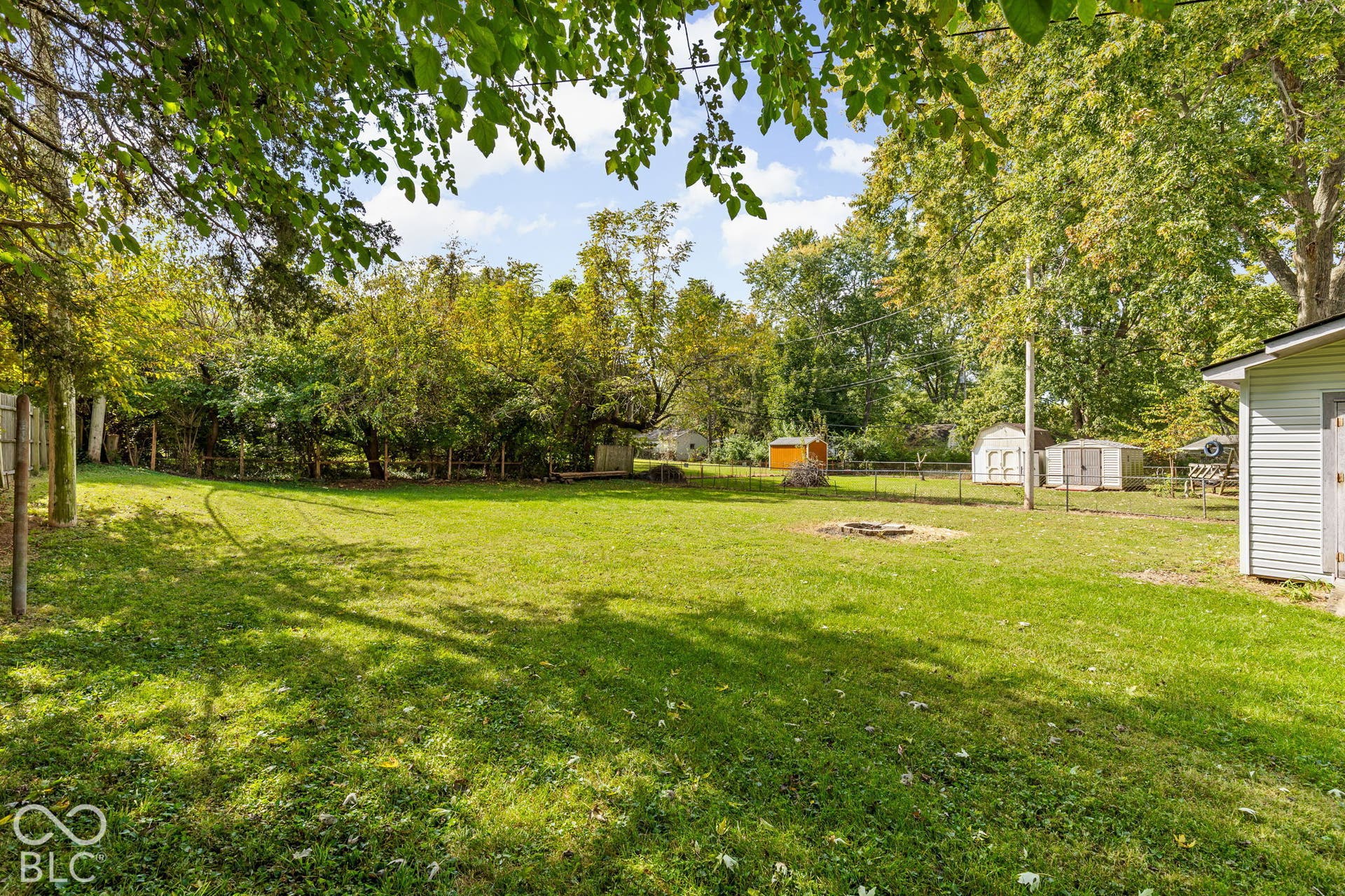 Expansive backyard featuring a fenced perimeter, mature trees, open lawn space, and two detached storage structures