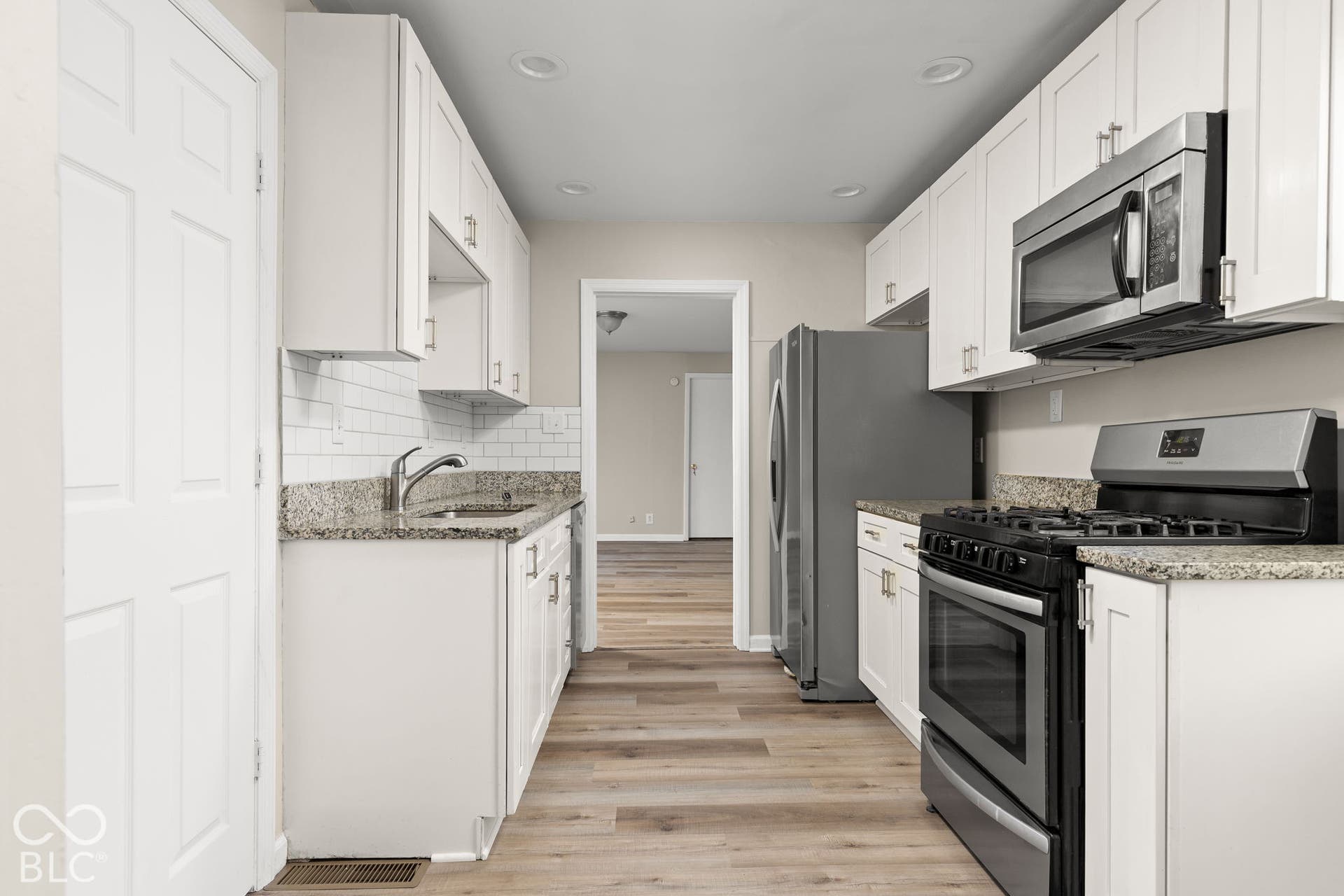 Kitchen featuring white shaker-style cabinetry, stone countertops, a subway tile backsplash, stainless steel appliances, and wood-finish flooring
