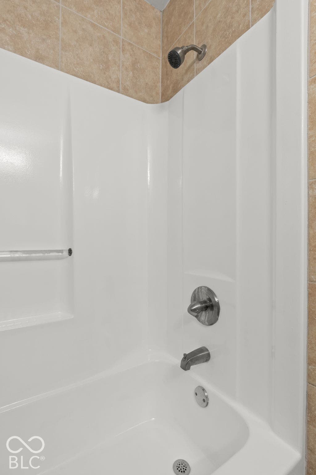 Shower and tub combination featuring a molded white surround, integrated shelving, metallic finish faucet hardware, and neutral-tone tile wall accents