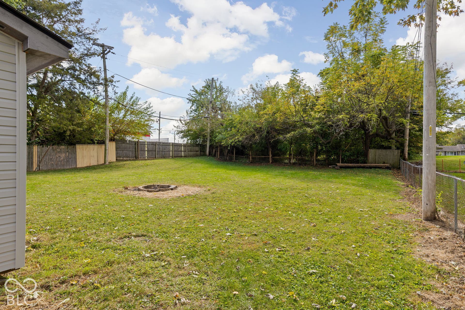 Expansive backyard featuring a lawn, a stone-lined fire pit, and partial wood and wire perimeter fencing