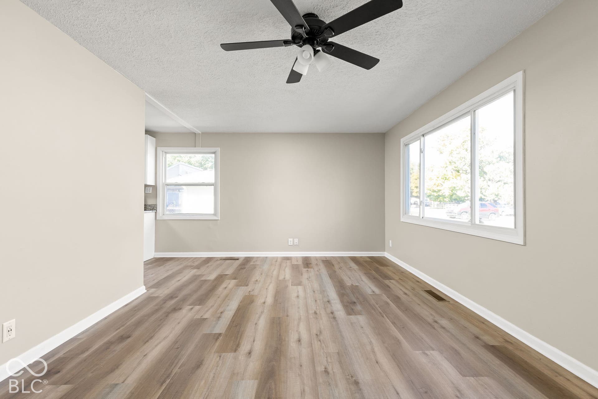 Neutral-toned interior featuring wood-finish flooring, dual-pane windows, and a matte black ceiling fan with an integrated light fixture