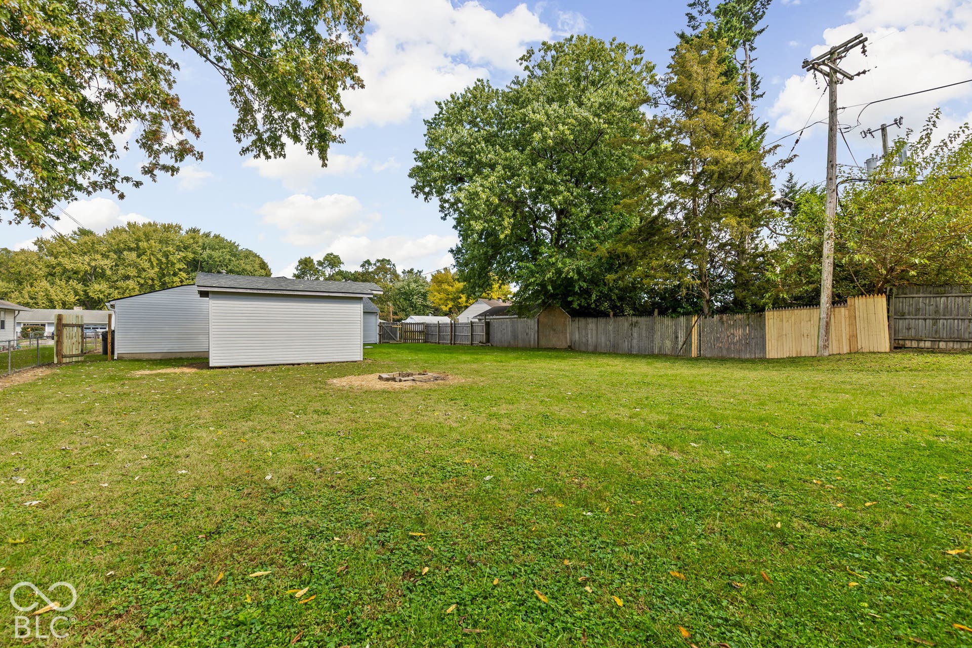 Expansive backyard featuring a level lawn, mature trees, wood privacy fencing, and a detached outbuilding