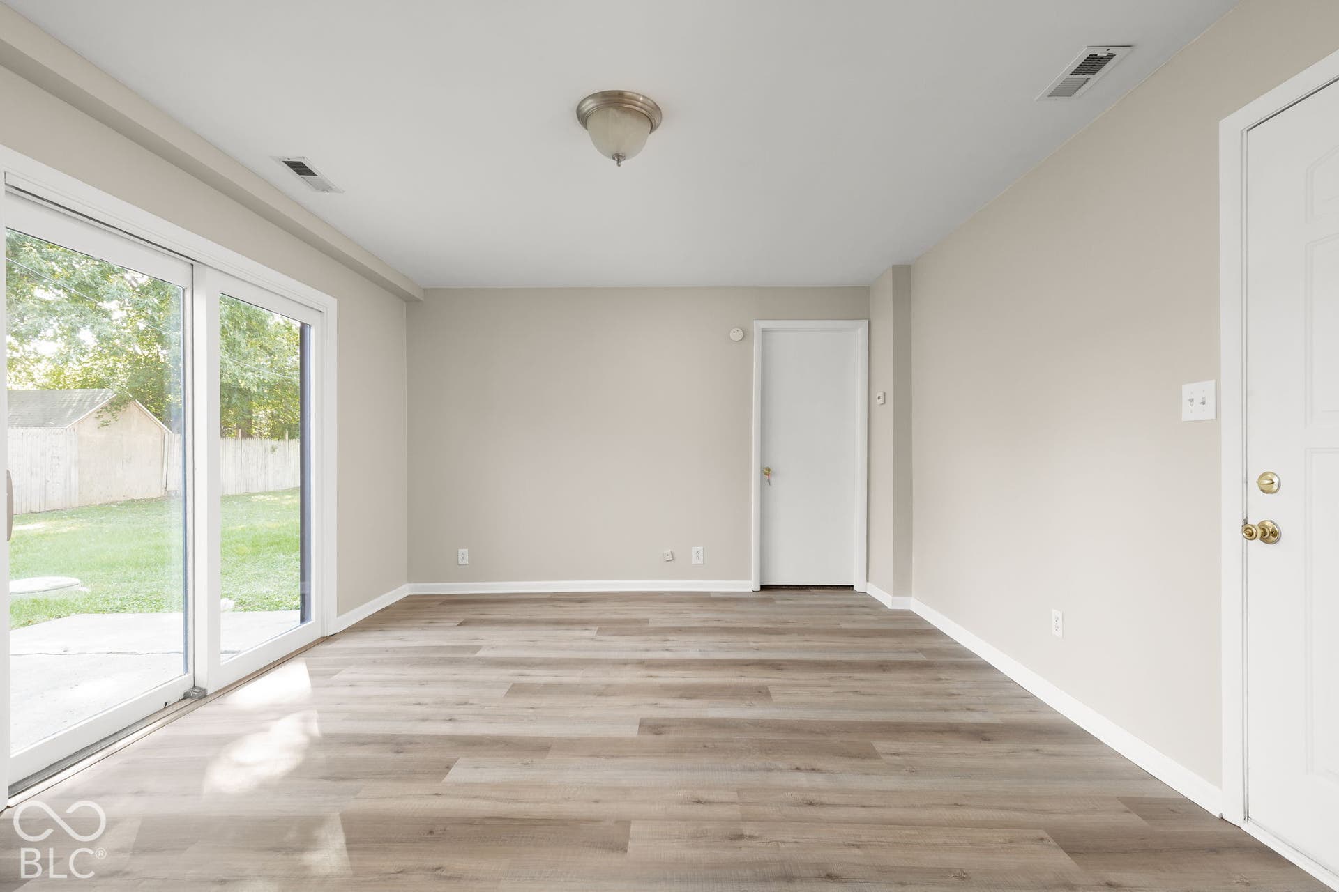 Neutral interior space featuring wood-finish flooring, sliding glass door, flush-mount ceiling lighting, and solid-core interior doors