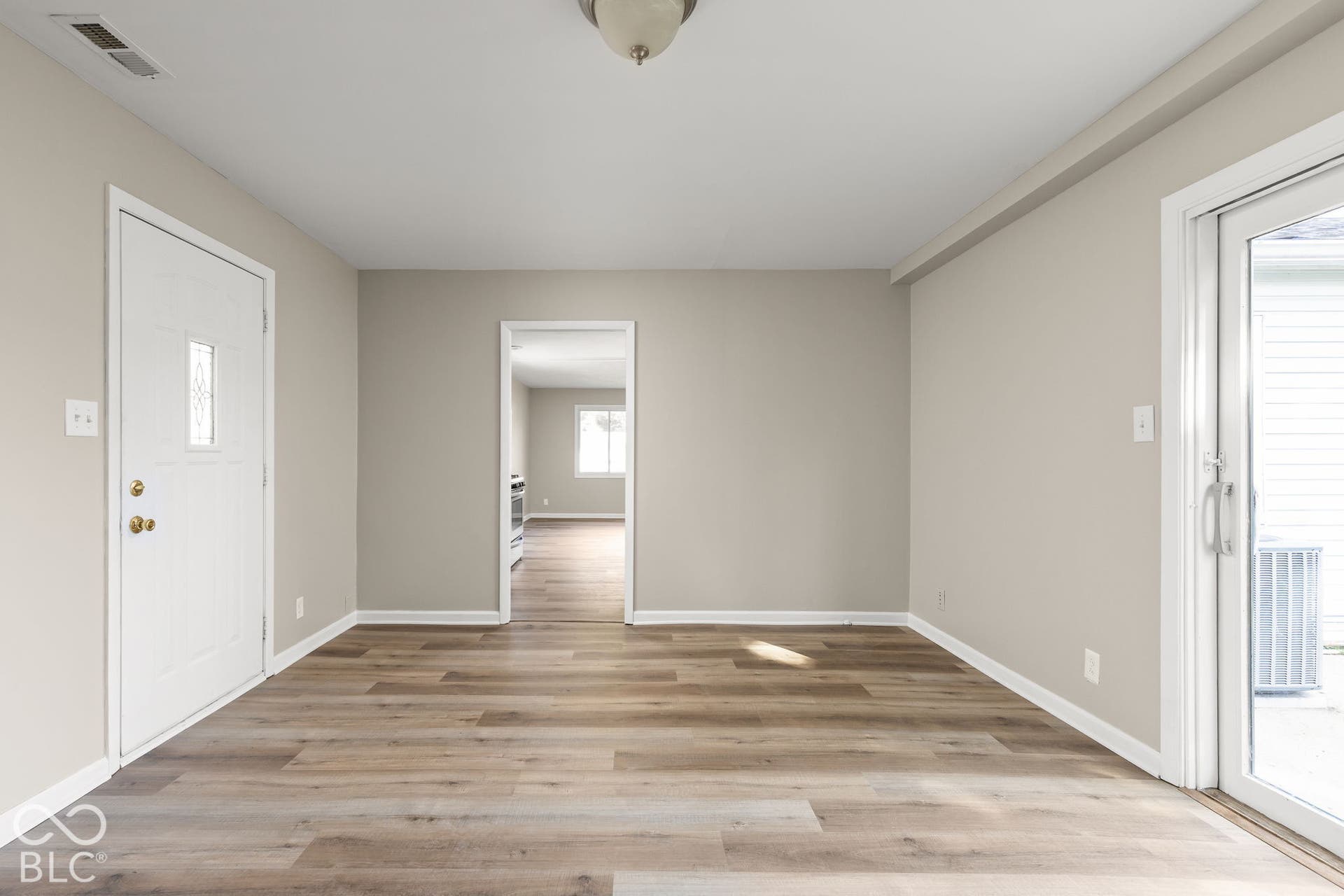 Neutral-toned interior featuring wood-finish flooring, a flush-mount light fixture, a six-panel exterior door, and a glass-paned sliding door