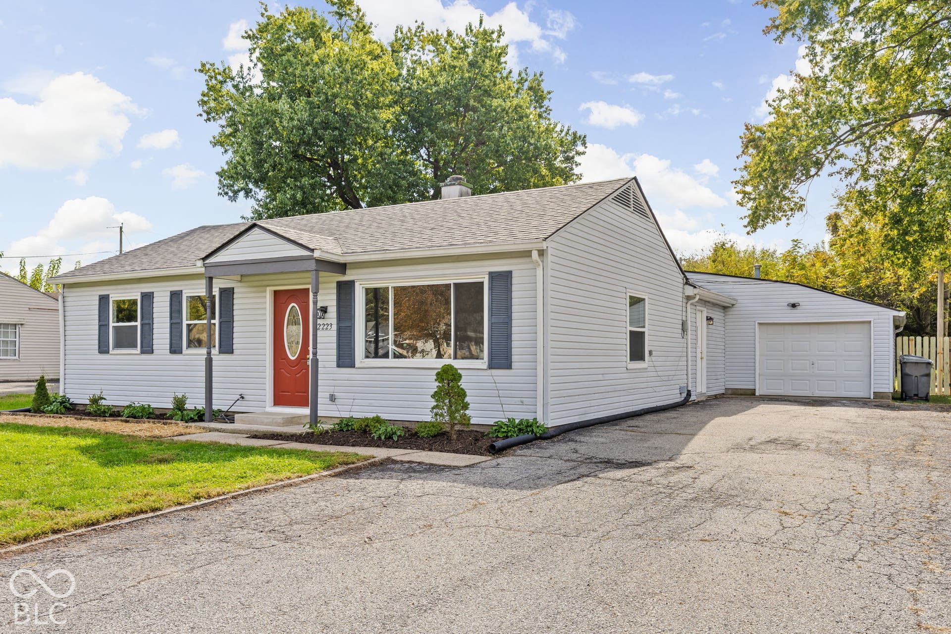 Single-story residence featuring light gray vinyl siding, dark blue exterior shutters, an asphalt-paved driveway, an attached garage, and a front entry with a covered porch