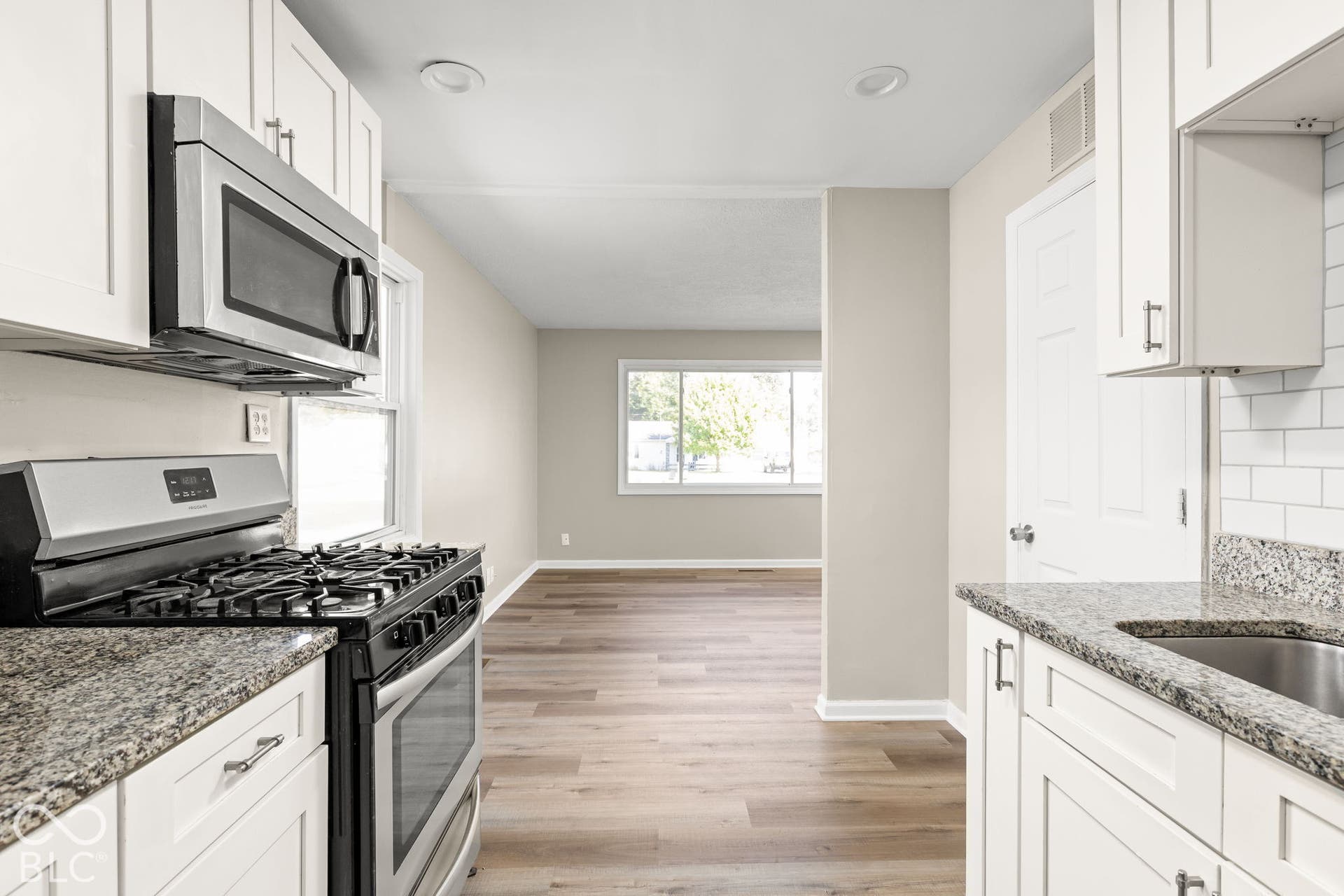 Kitchen featuring white shaker-style cabinetry, stone-finish countertops, subway tile backsplash, stainless steel gas range and microwave, and wood-finish flooring