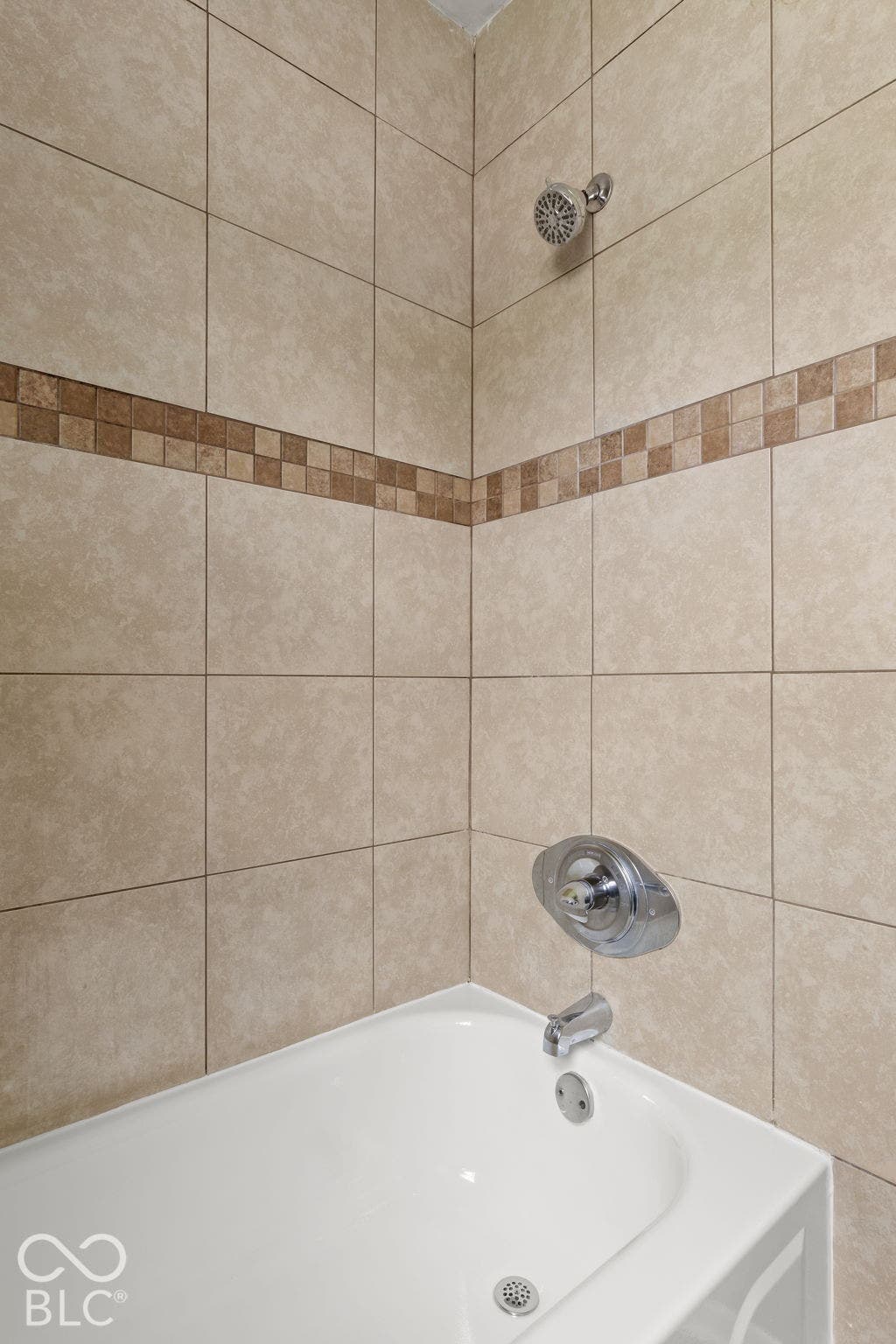 Tub shower combination featuring neutral-toned wall tile, a decorative mosaic tile accent border, and chrome plumbing fixtures