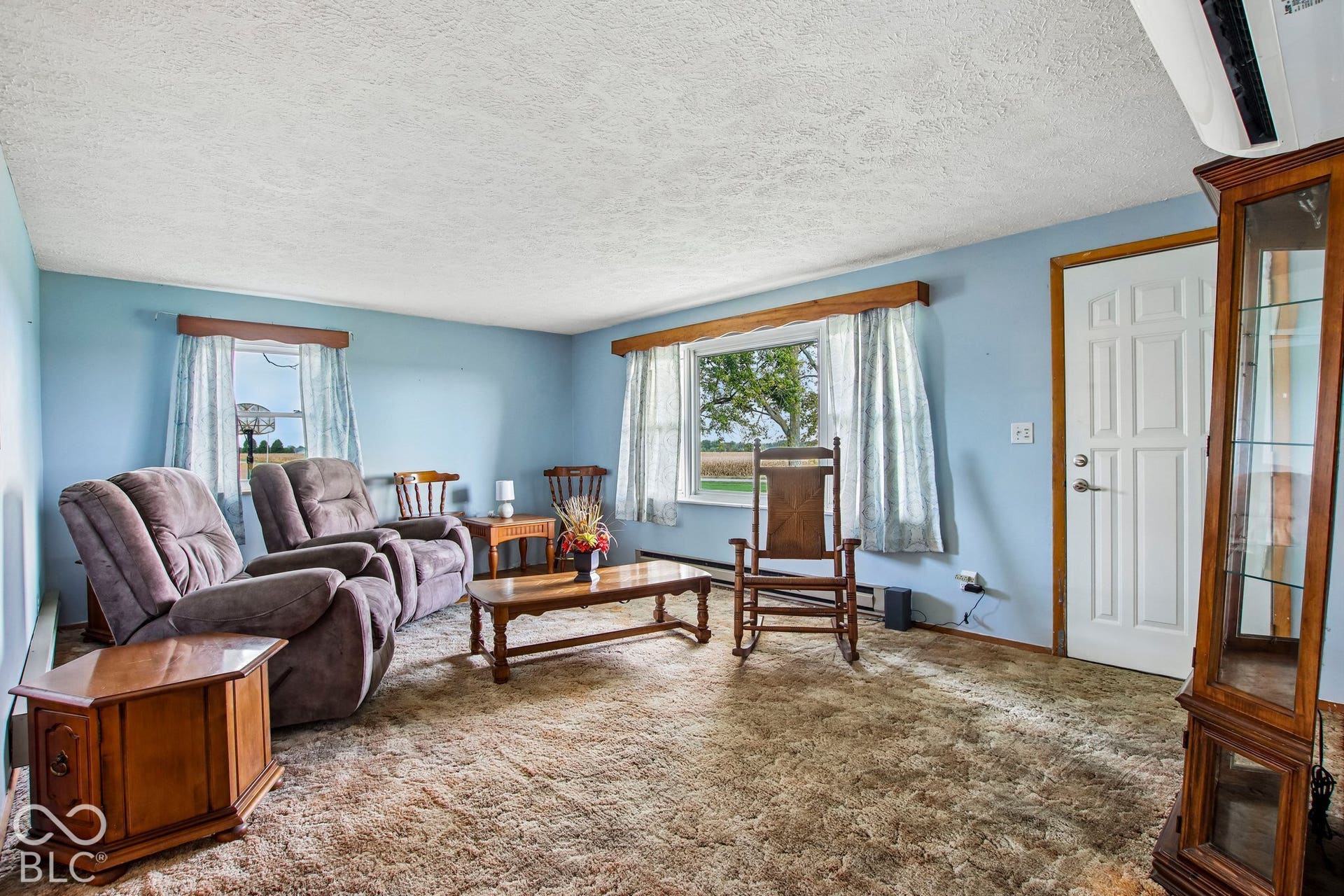 4469 E 400 S, Franklin, IN 46131 Living area featuring dual picture windows with wood trim, wall-mounted air conditioning unit, and textured ceiling