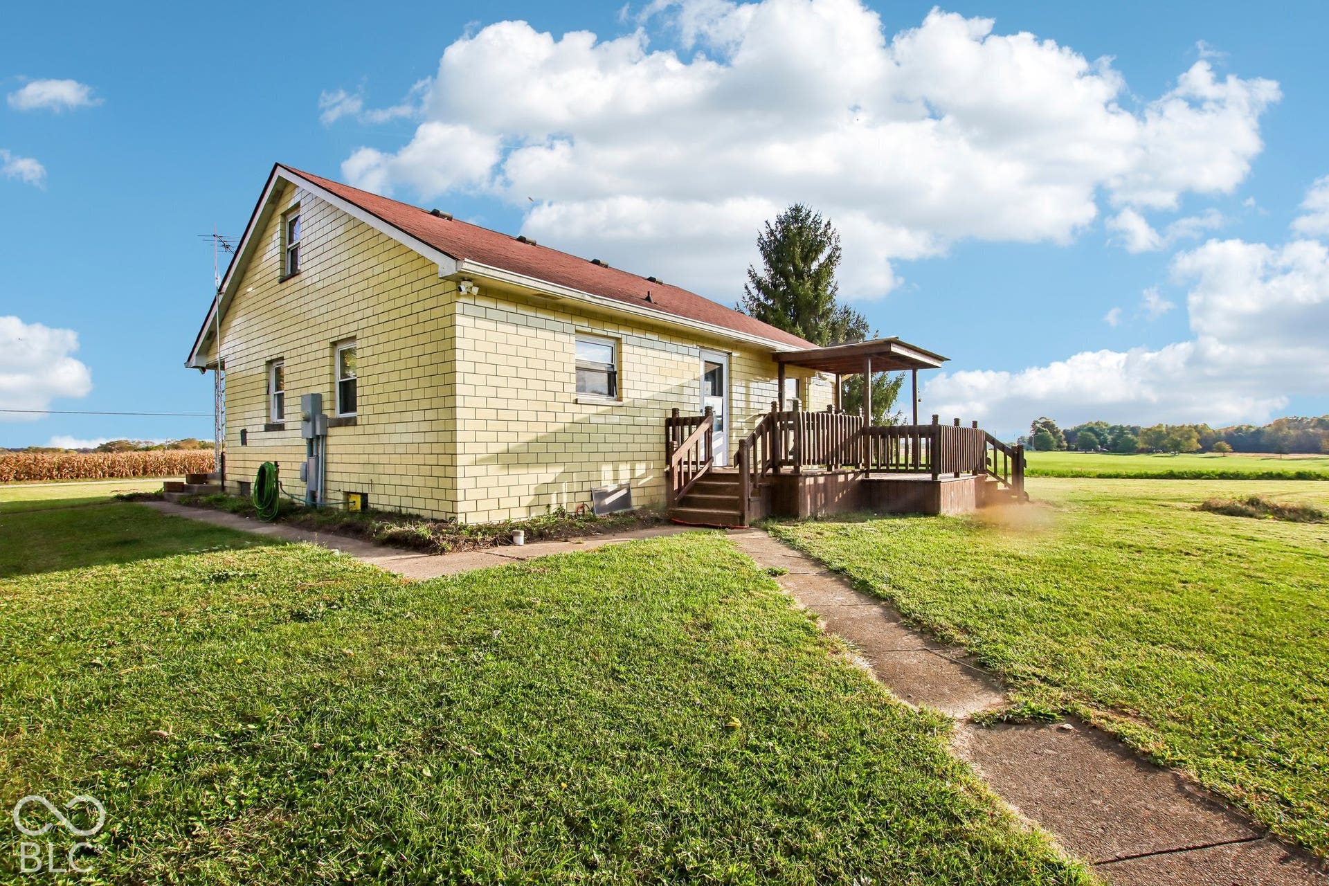 4469 E 400 S, Franklin, IN 46131 Exterior featuring yellow masonry siding, a red shingle roof, a raised wood deck, and an expansive lawn
